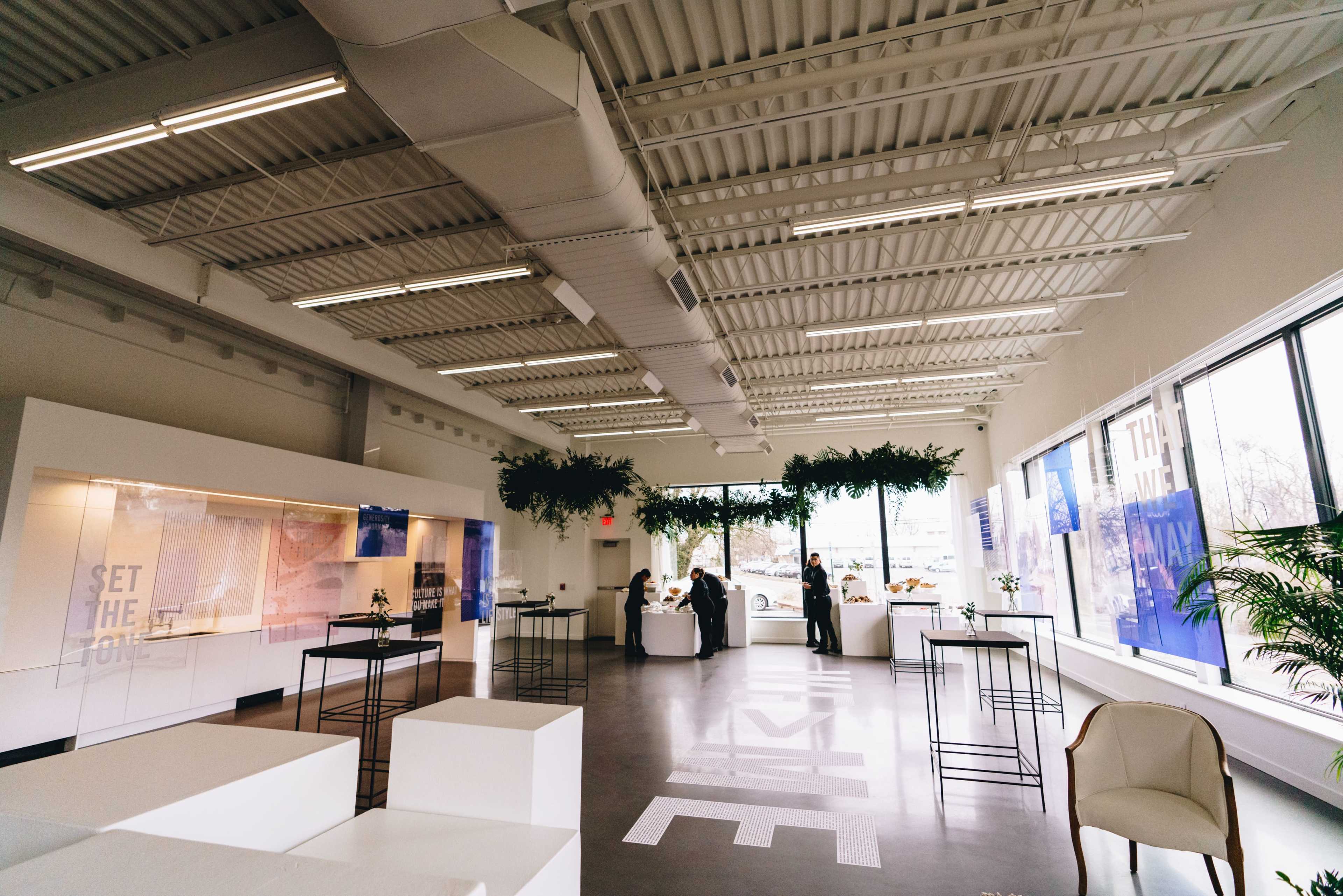 The interior of a modern showroom features white walls, large windows, and minimalistic furniture arranged in a spacious layout.