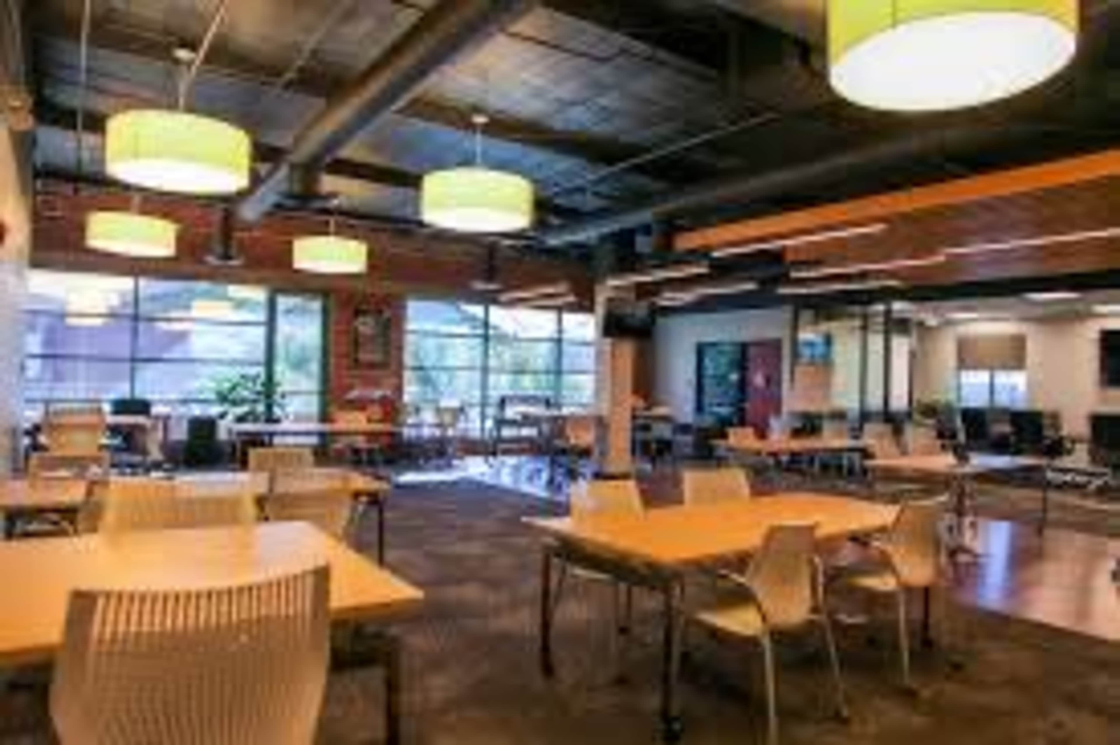 A modern office or co-working space with several tables, chairs, and large windows allowing natural light to fill the room.