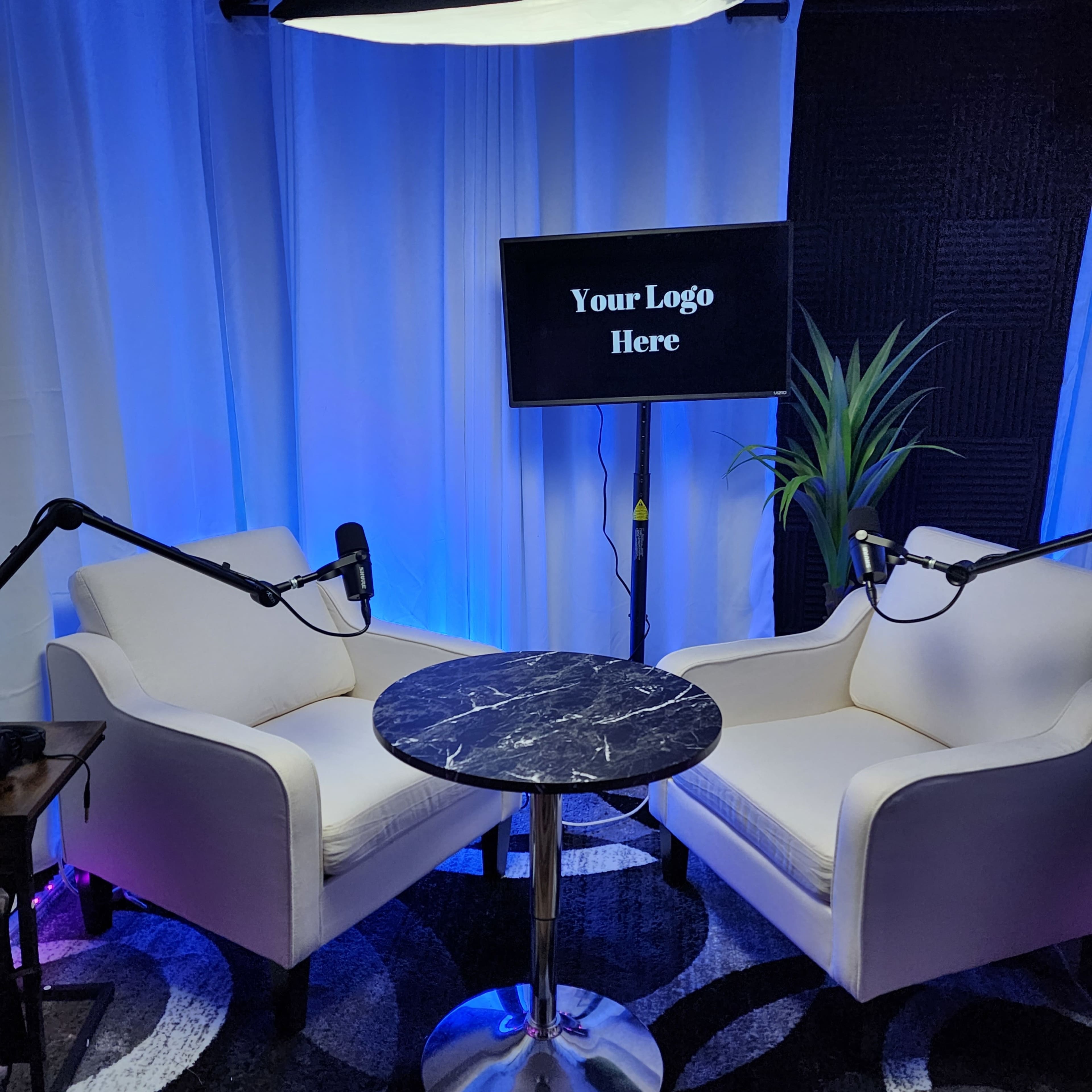 A podcast or interview setup features two white chairs, a round marble table, and a monitor displaying "Your Logo Here," all set against a backdrop of white fabric and colored lighting.