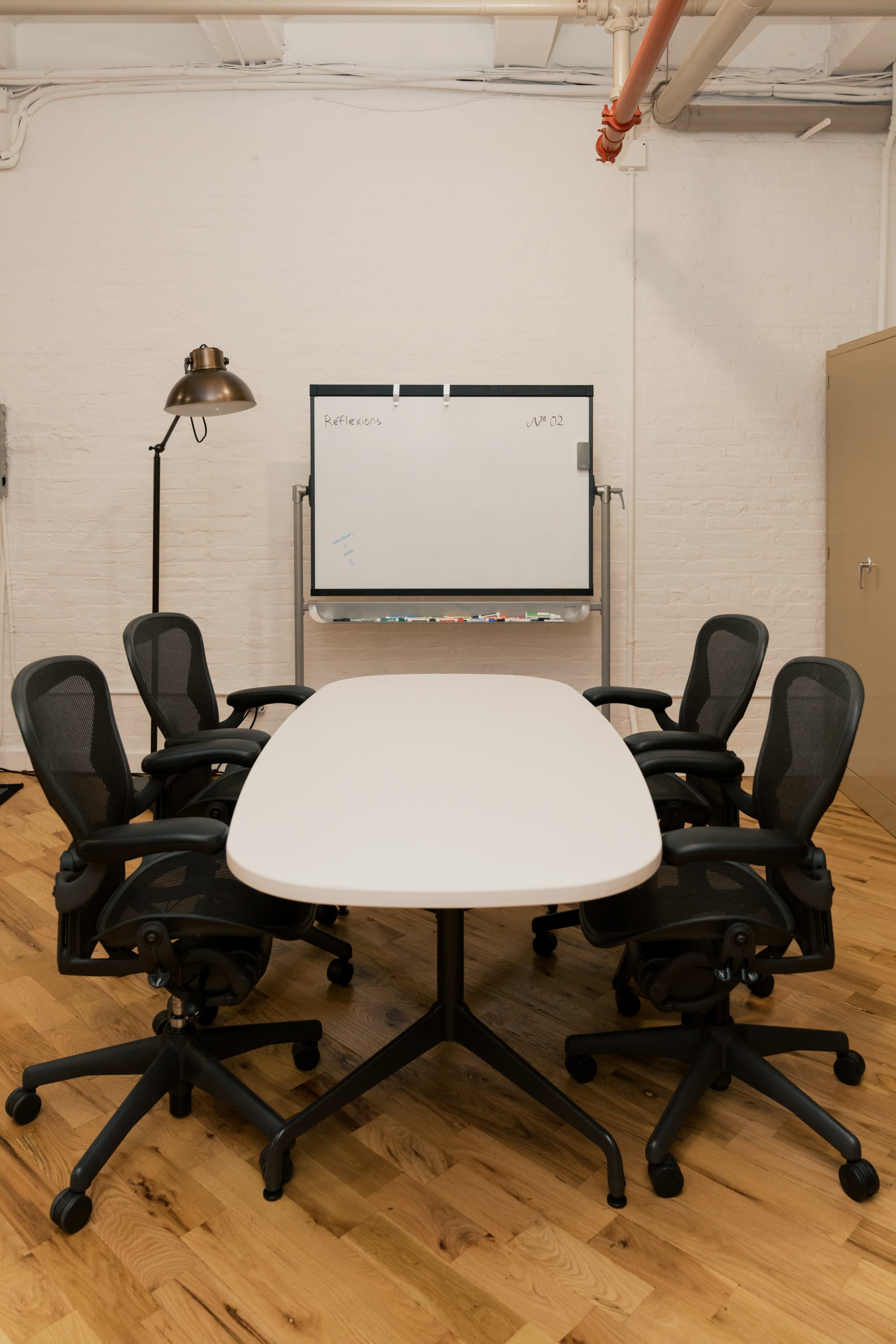 A conference room features a white oval table surrounded by five ergonomic chairs, with a whiteboard mounted on a wall in the background.