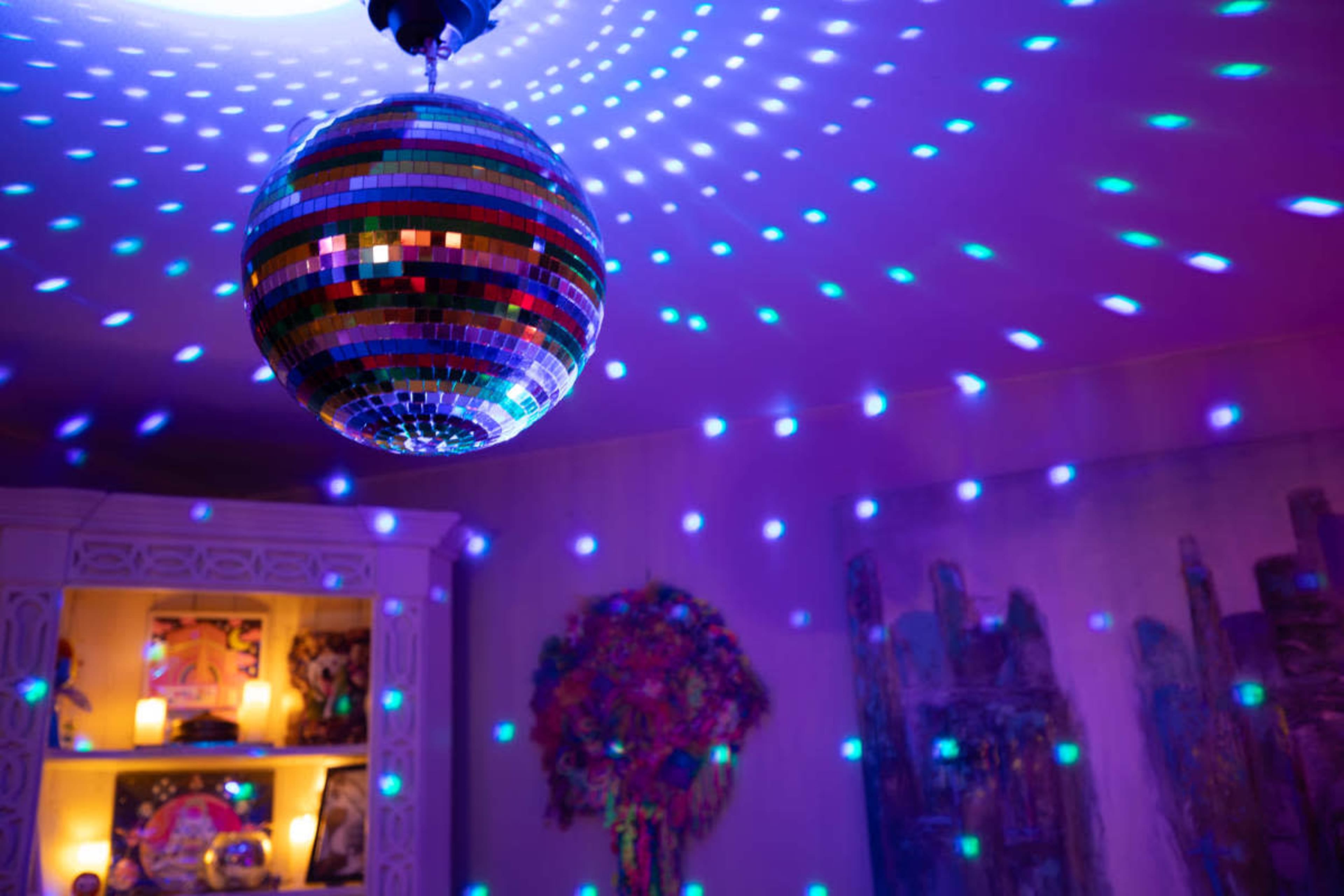A disco ball reflects multicolored lights onto the walls and ceiling of a dimly lit room.