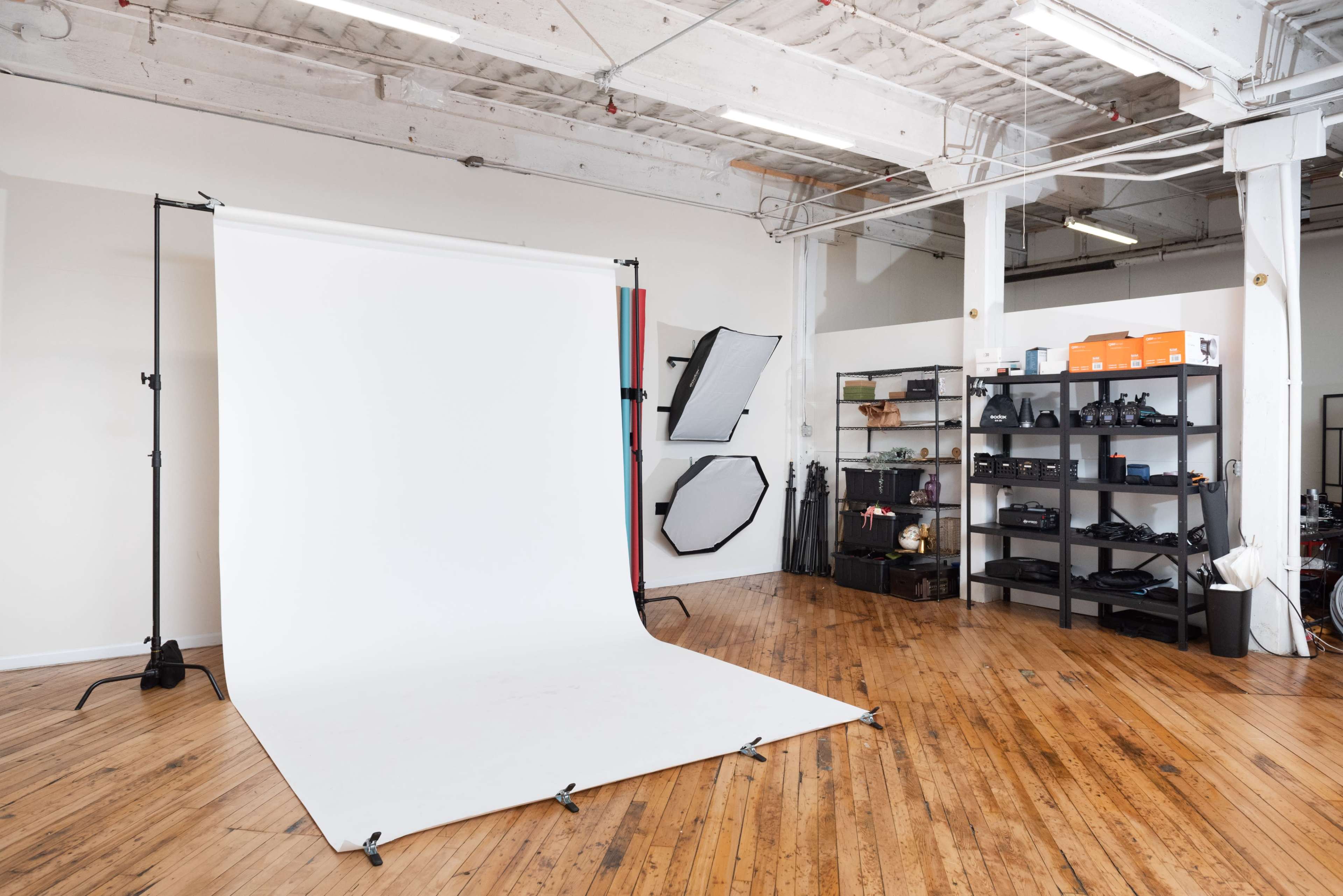 A photography studio with a white backdrop, multiple light reflectors mounted on a wall, and shelves filled with camera equipment.