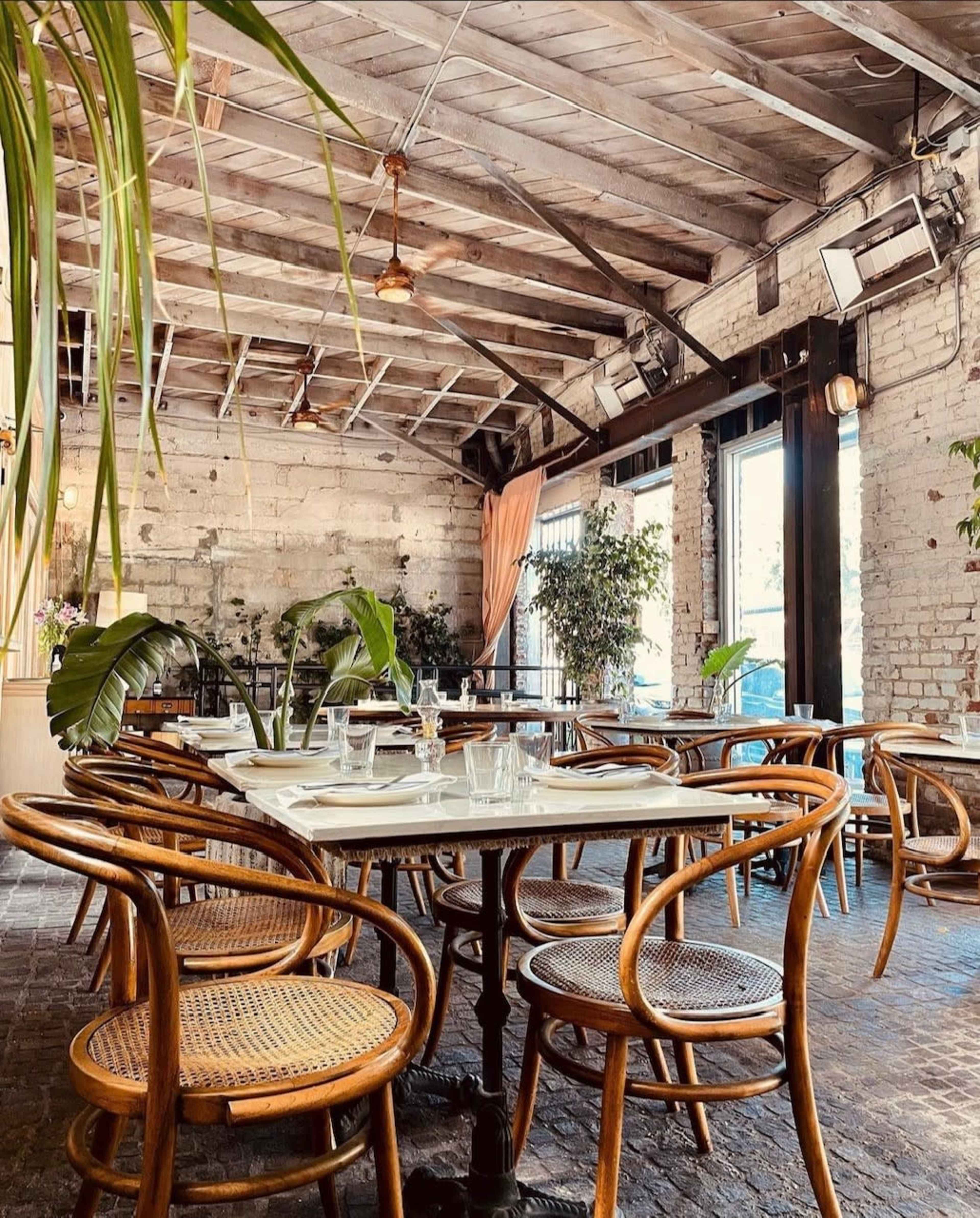 A cozy restaurant interior with wooden beams, wicker chairs, and tables set for dining.