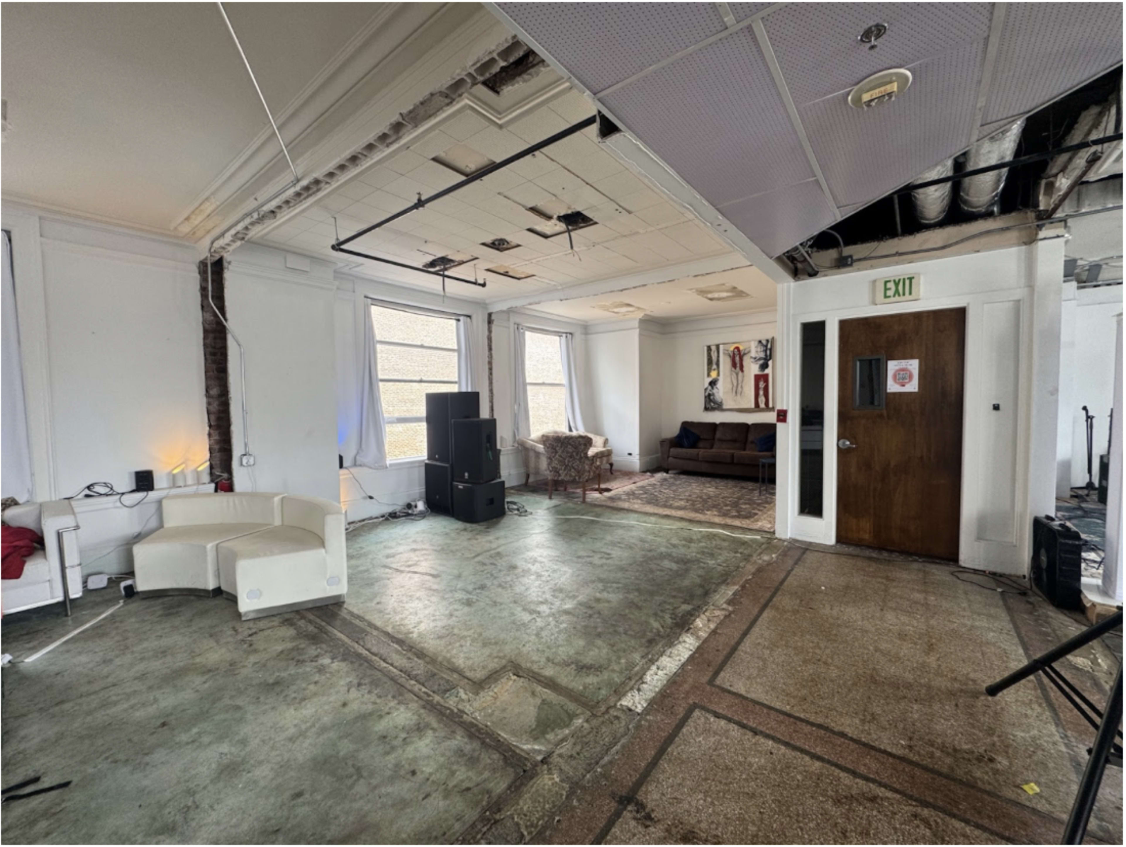 The image shows an unfinished indoor space with bare concrete flooring, two windows, and a couch in one corner.