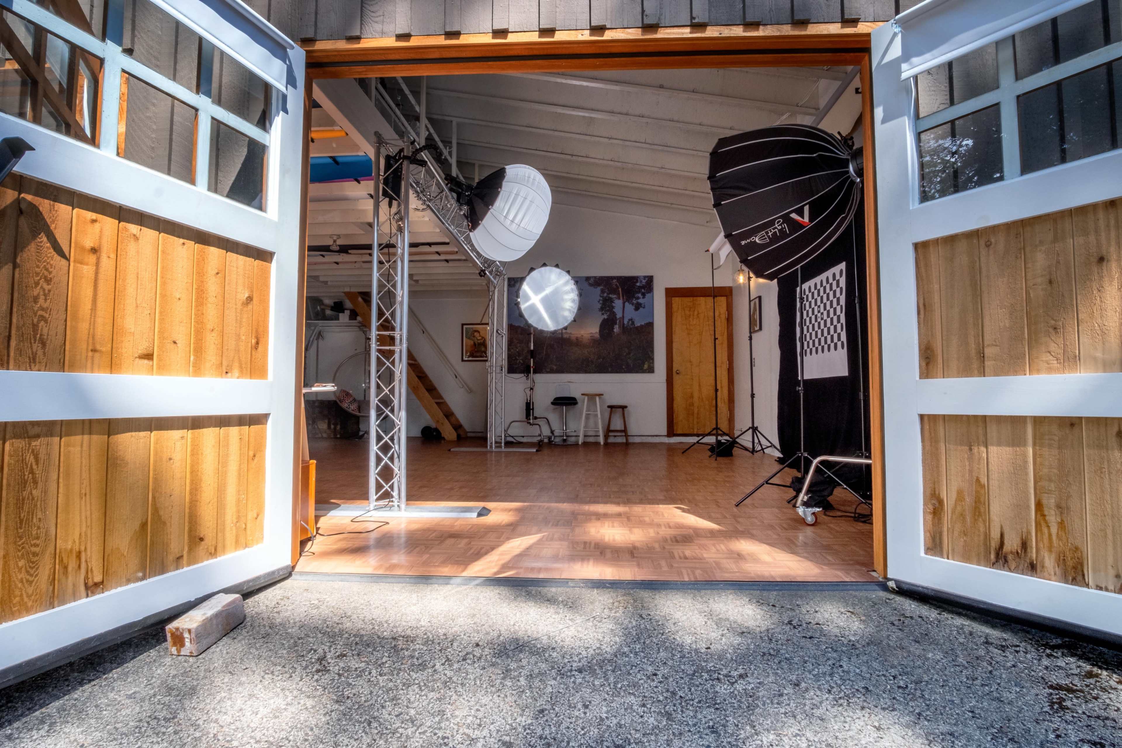 An open garage door leading into a photography studio equipped with lighting equipment and wooden floors.