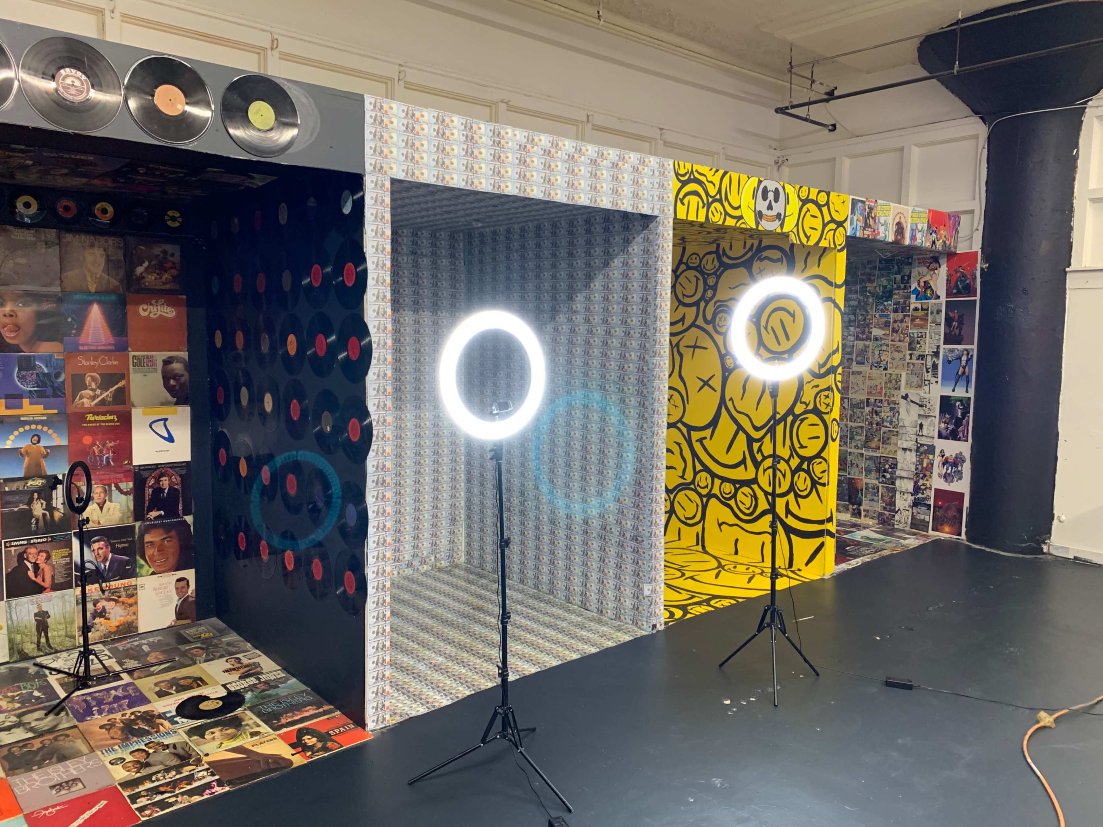 A room with three decorated walls featuring colorful patterns and graphics, with two ring lights set up on stands in front.