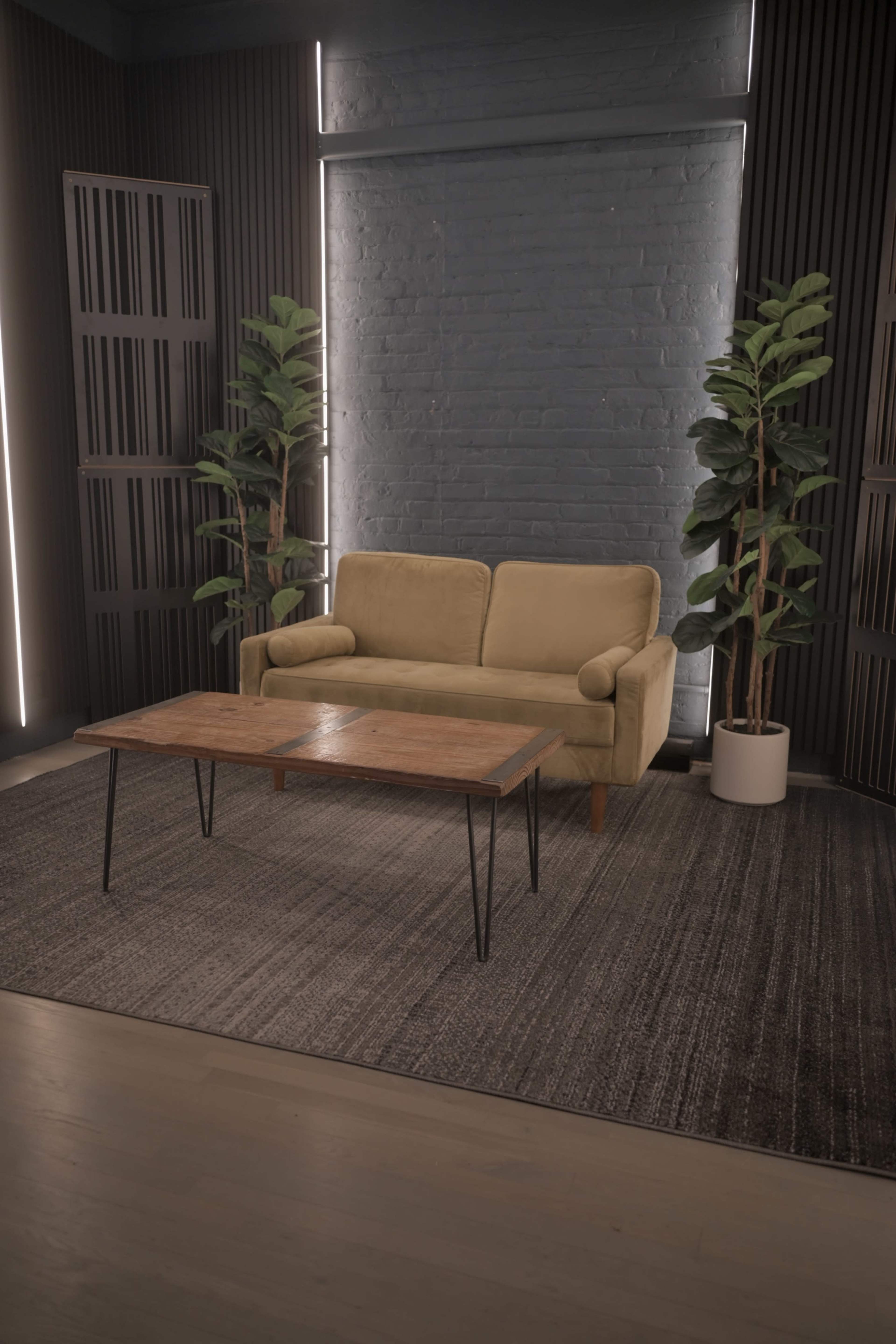 A beige sofa and a wooden coffee table are positioned on a textured rug in a well-lit room featuring potted plants and dark paneling.