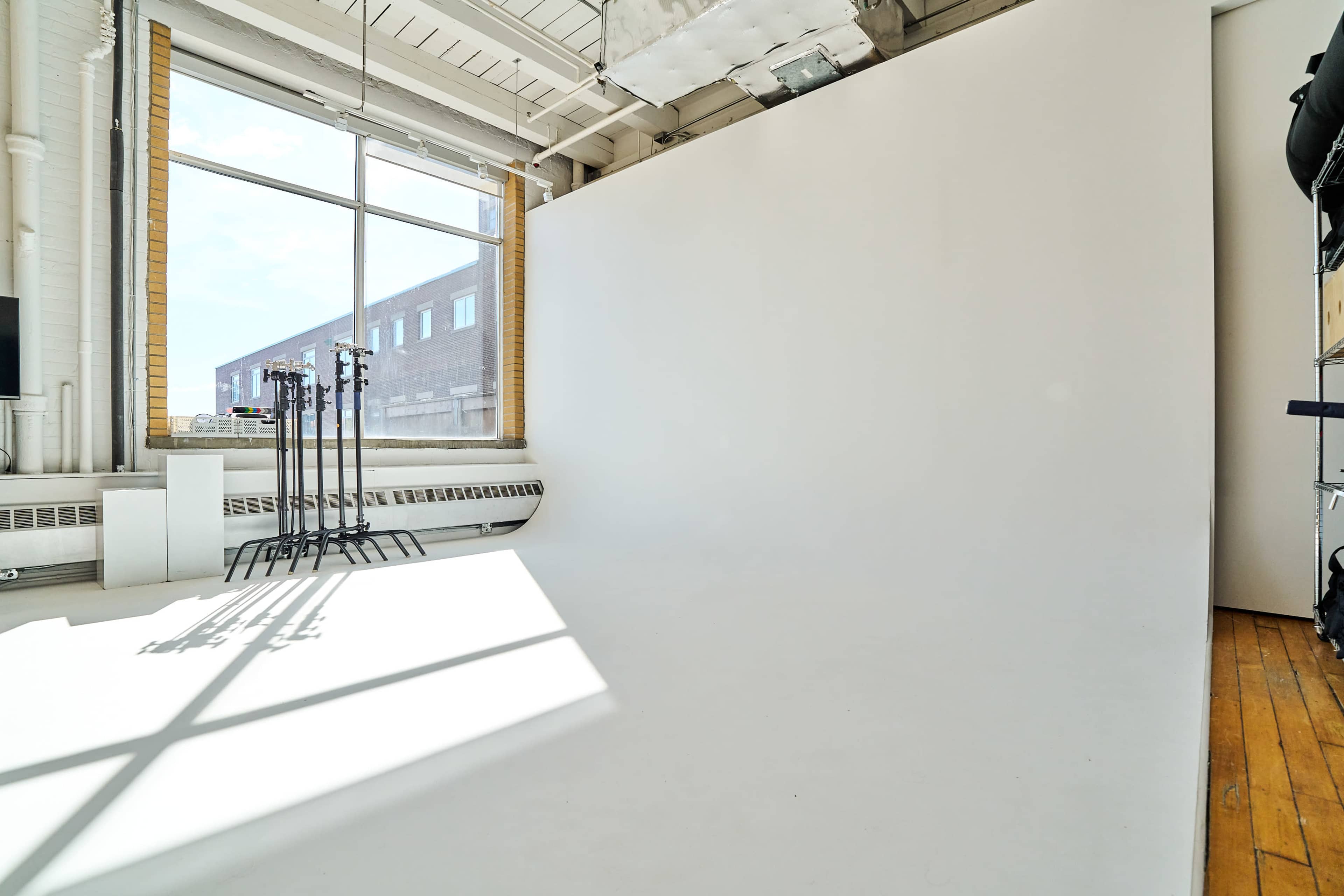 A bright photography studio with a large window and a seamless white backdrop.