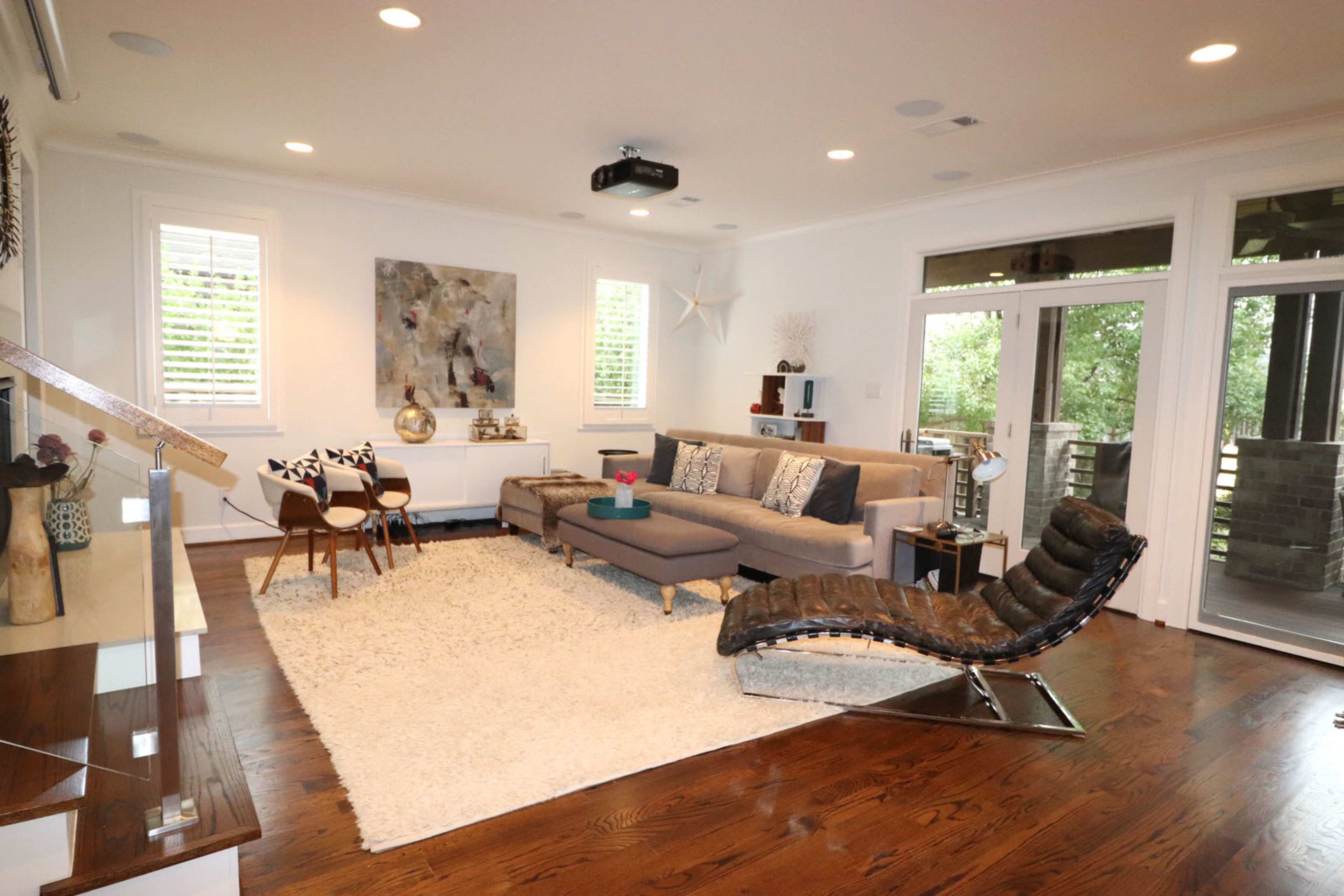 A modern living room features a sectional sofa, a sleek lounge chair, a large area rug, and glass doors leading to an outdoor space.