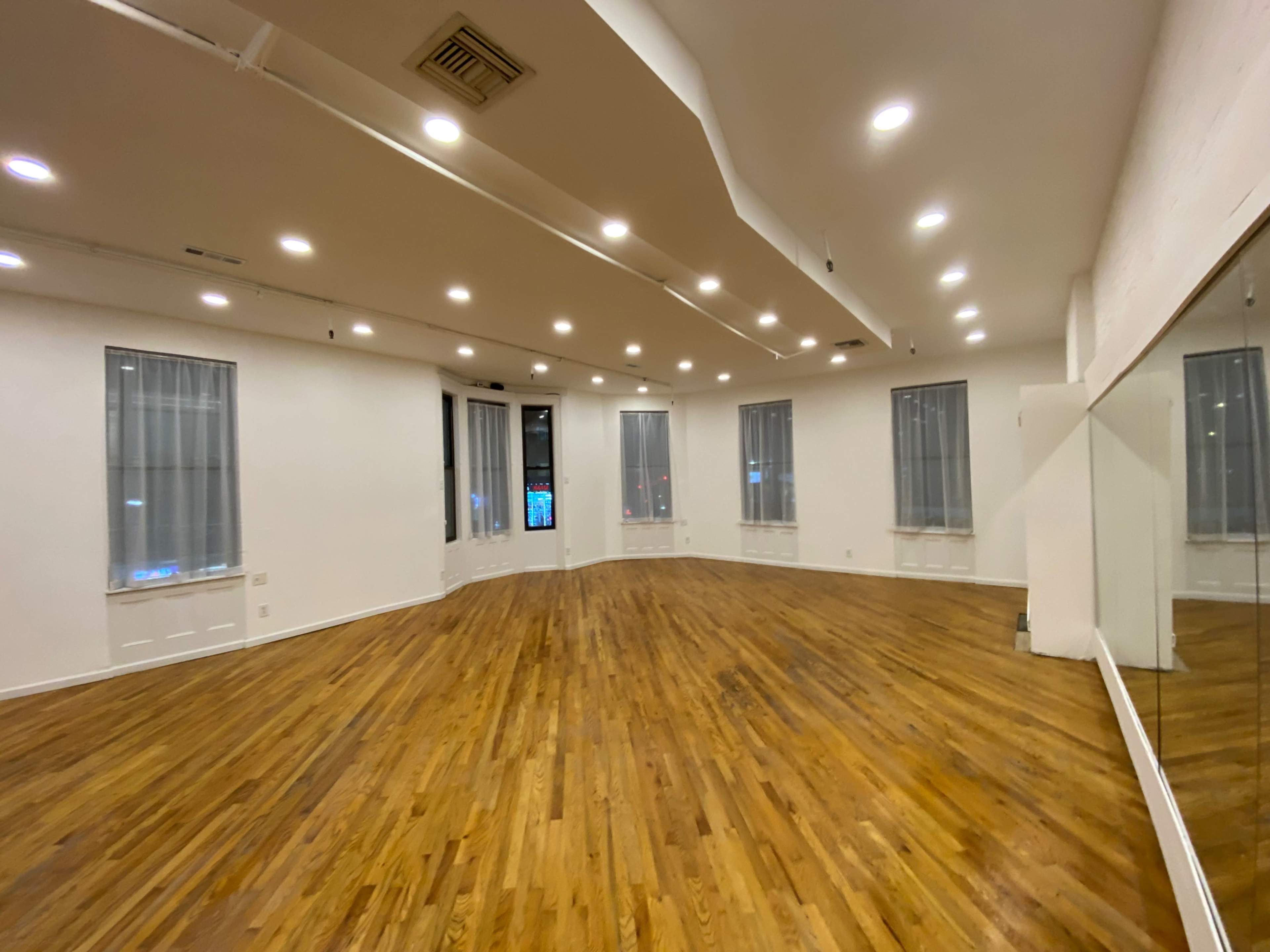 The room features hardwood flooring, white walls, large windows, and a wall-mounted mirror.