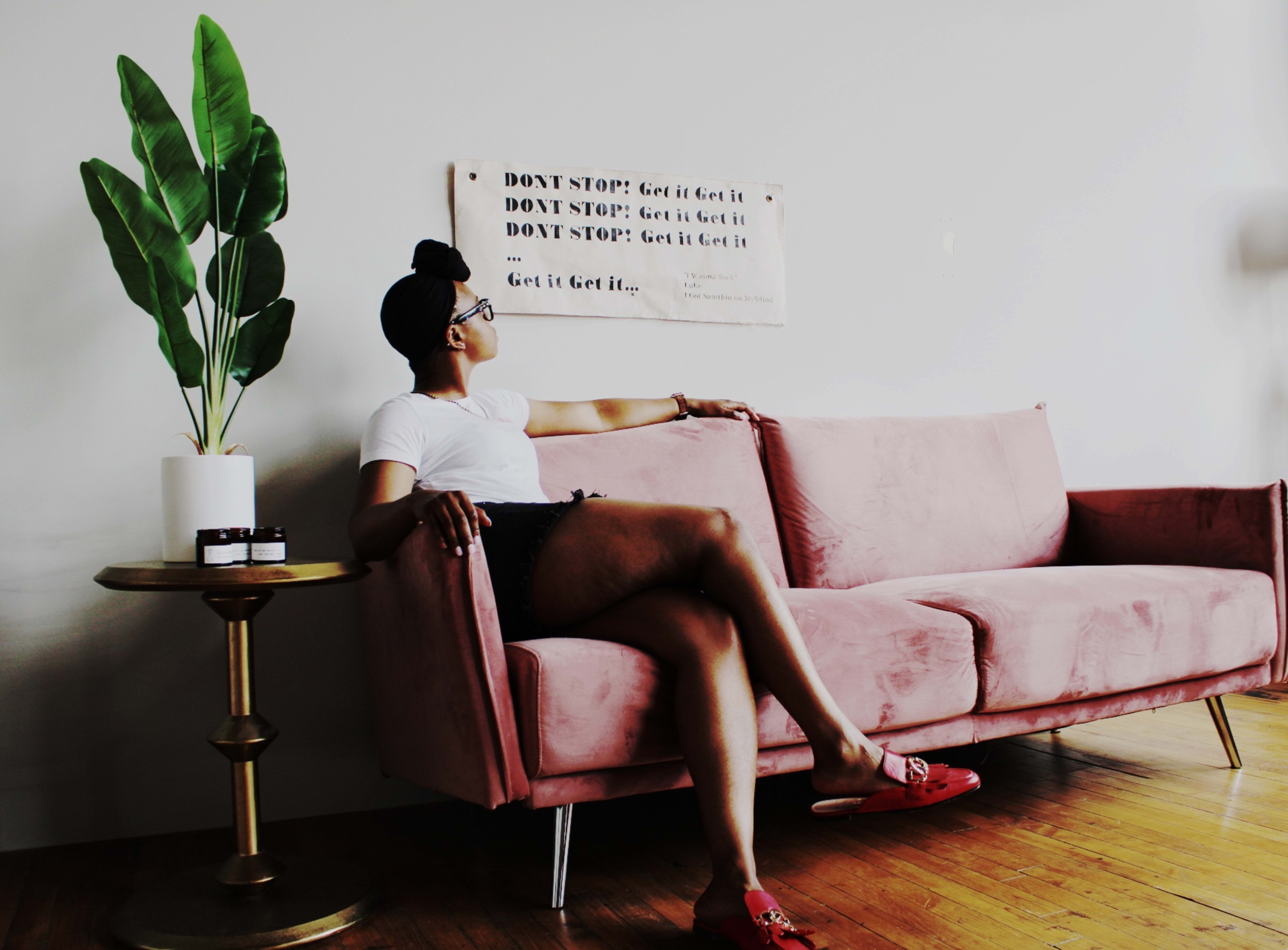 A profile of a person sitting on a pink couch next to a potted plant.