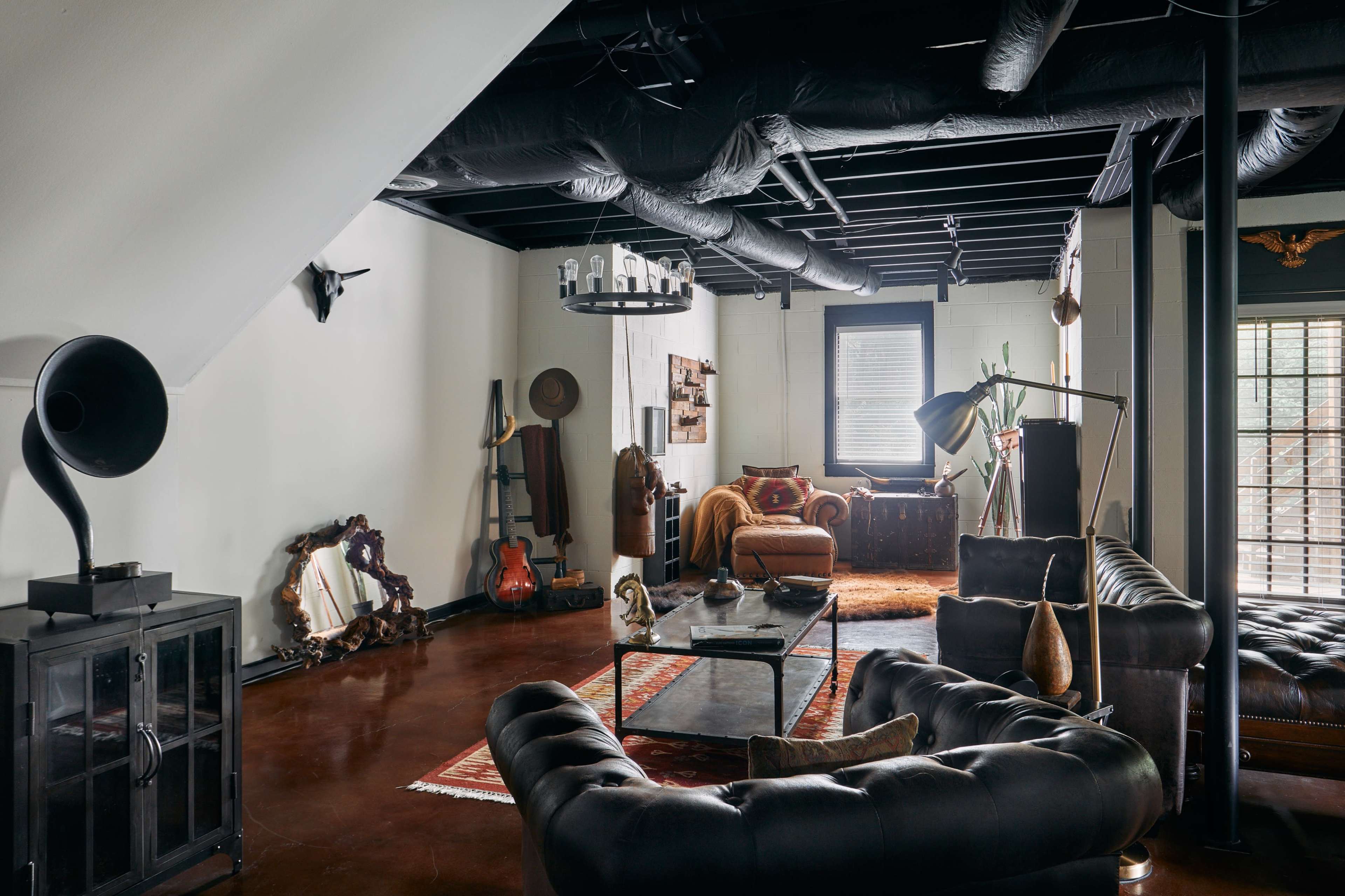 A spacious living room featuring dark leather sofas, a large coffee table, various decorative items, and a combination of industrial and vintage decor elements.
