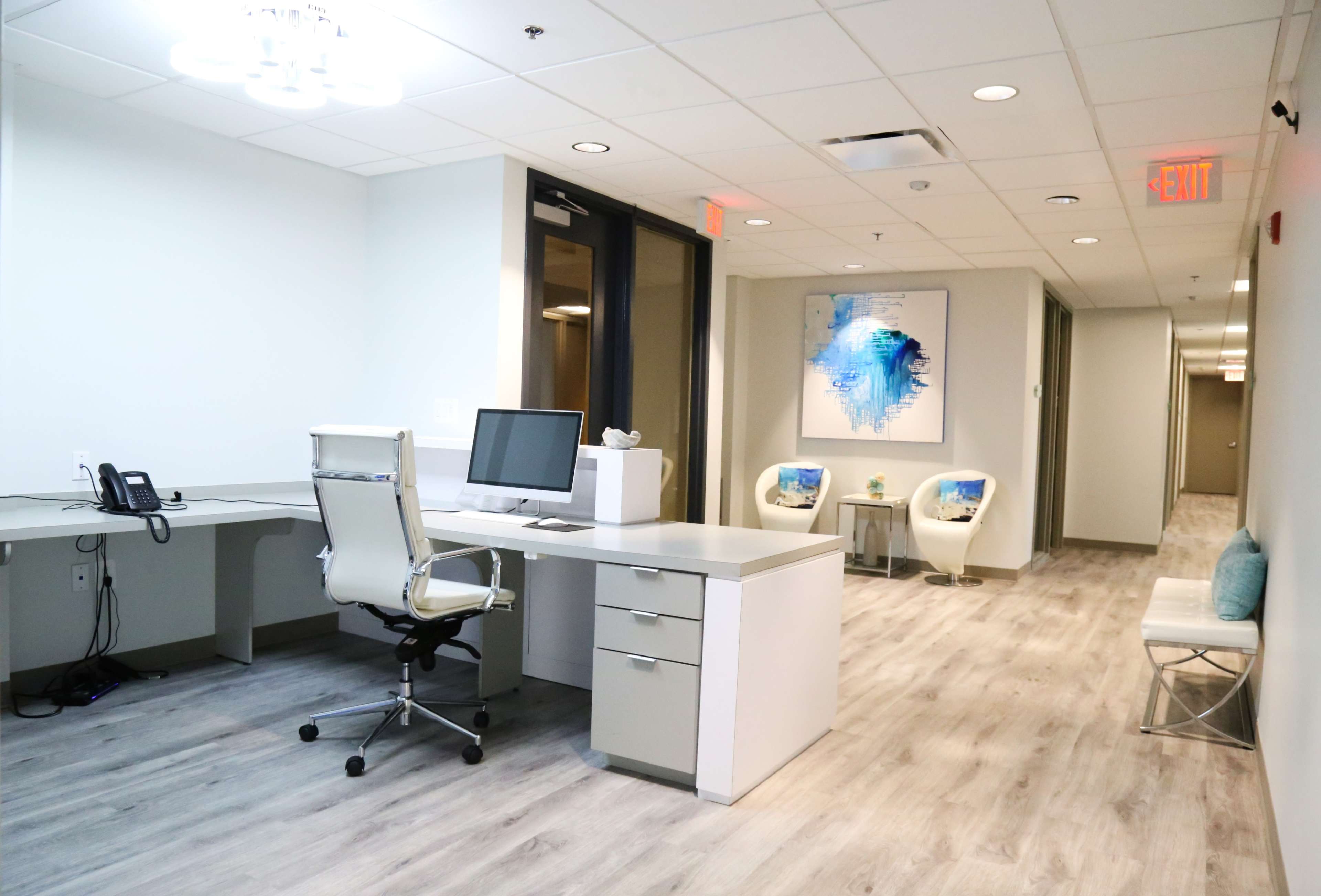 A modern office space with a desk, computer, and seating area along a well-lit corridor.