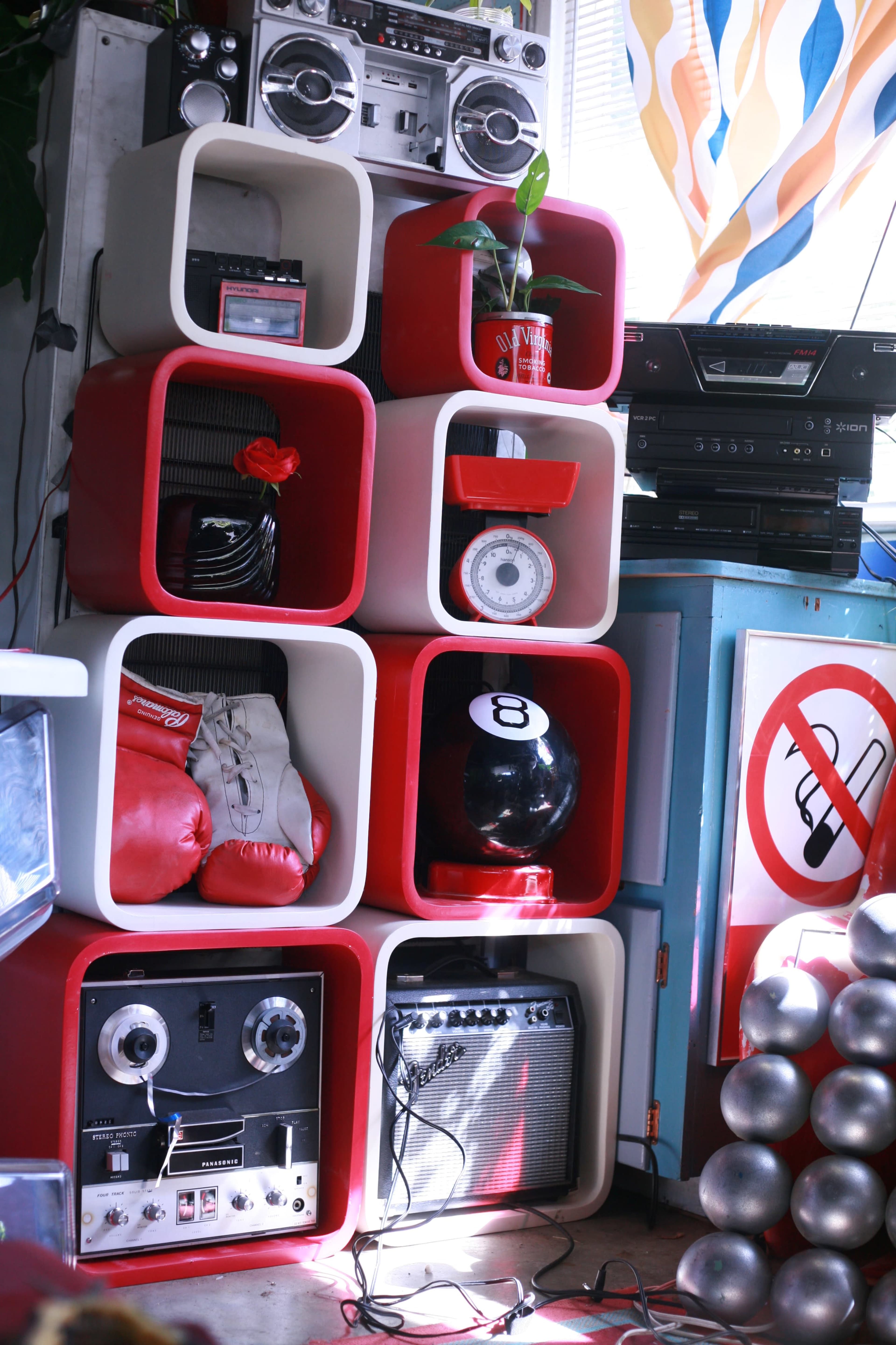 A colorful arrangement of retro storage cubes filled with various items, including boxing gloves, a plant, an eight-ball, and vintage audio equipment.