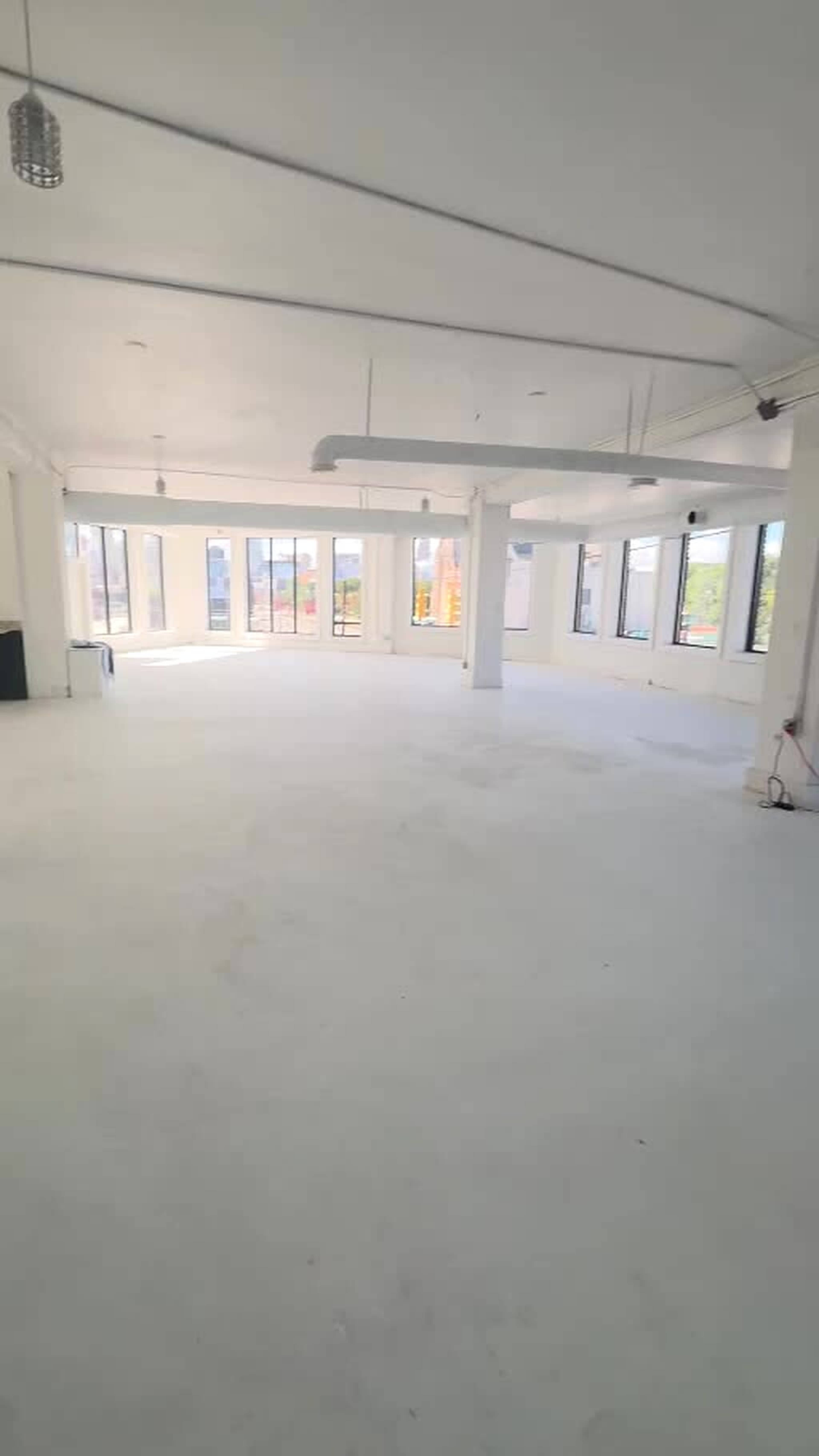 The image shows a spacious, empty room with large windows and a white floor.