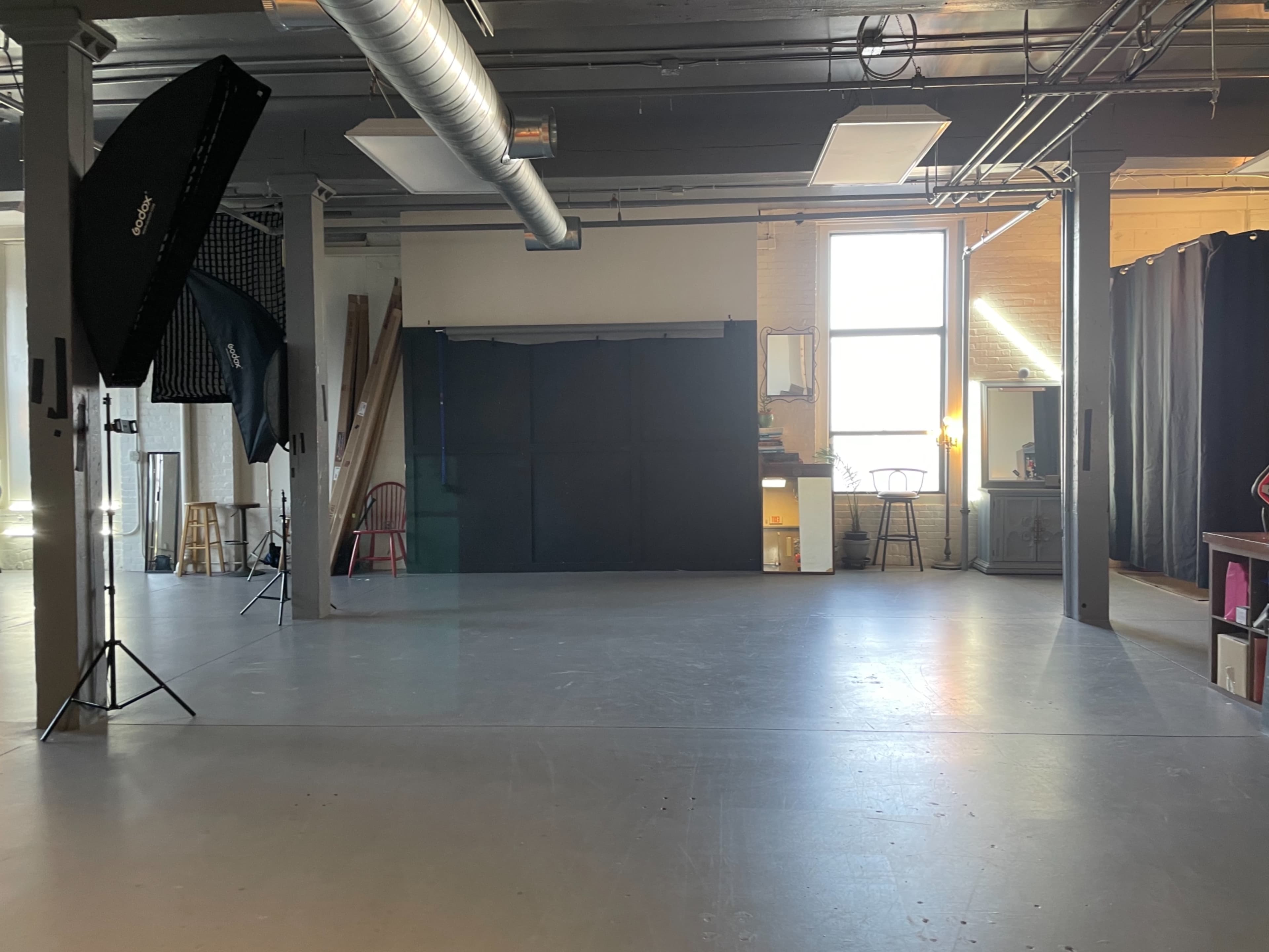 An empty studio space with photography equipment, large windows, and various props scattered around.