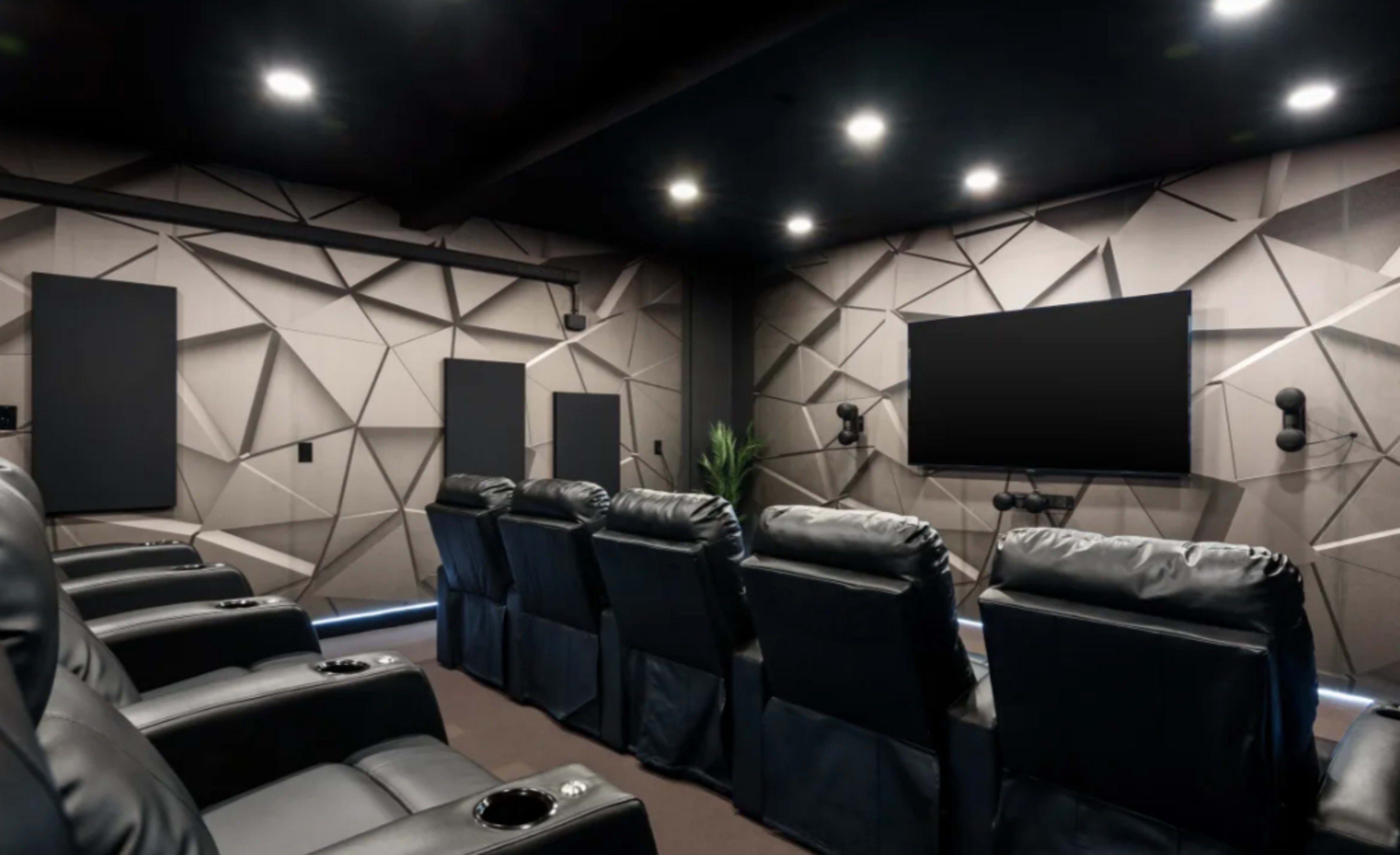 A modern home theater with black recliner seating, a flat-screen TV on the wall, and textured acoustic panels.