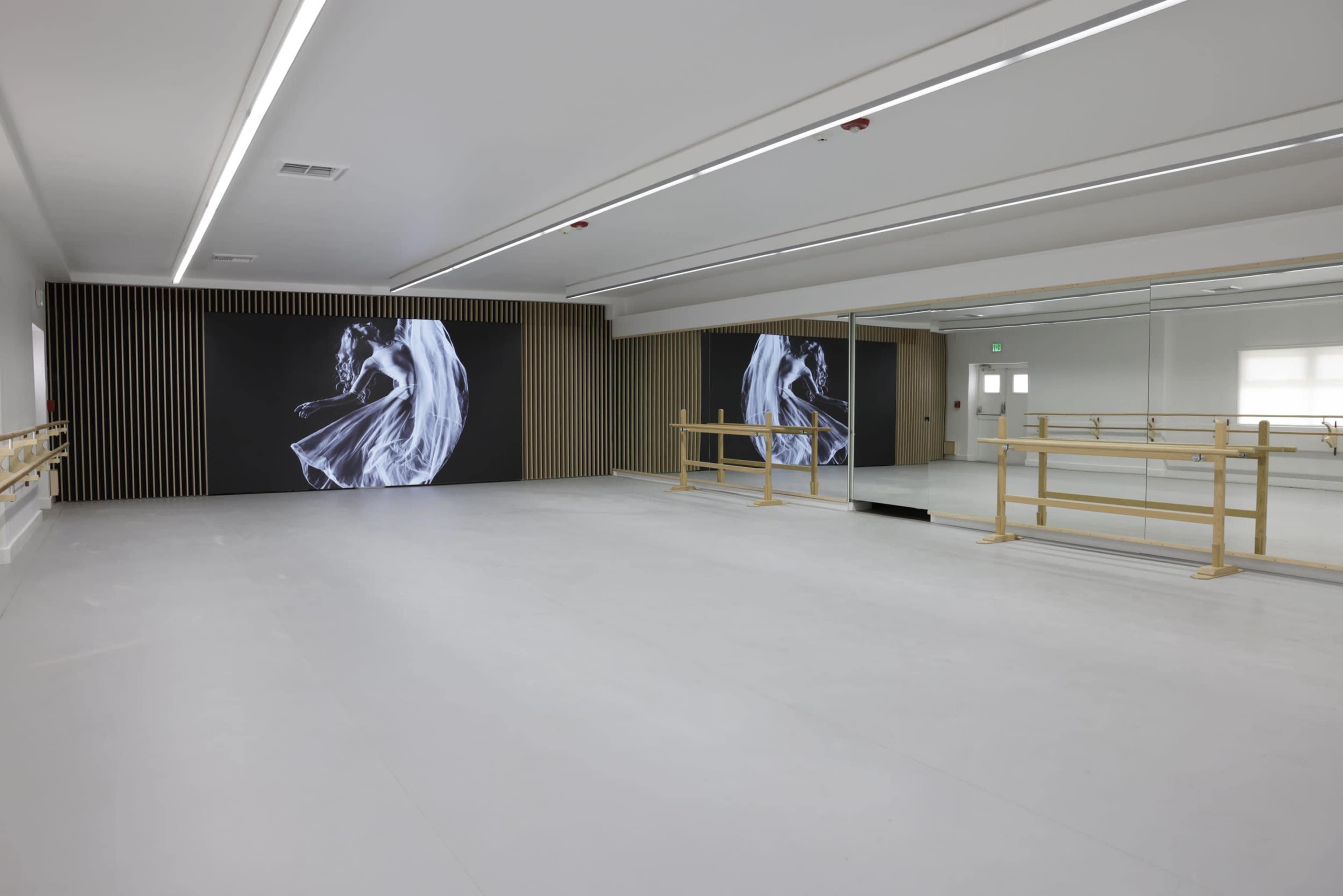 A spacious dance studio with a mirrored wall, wooden ballet barres, and an abstract artwork displayed on one side.