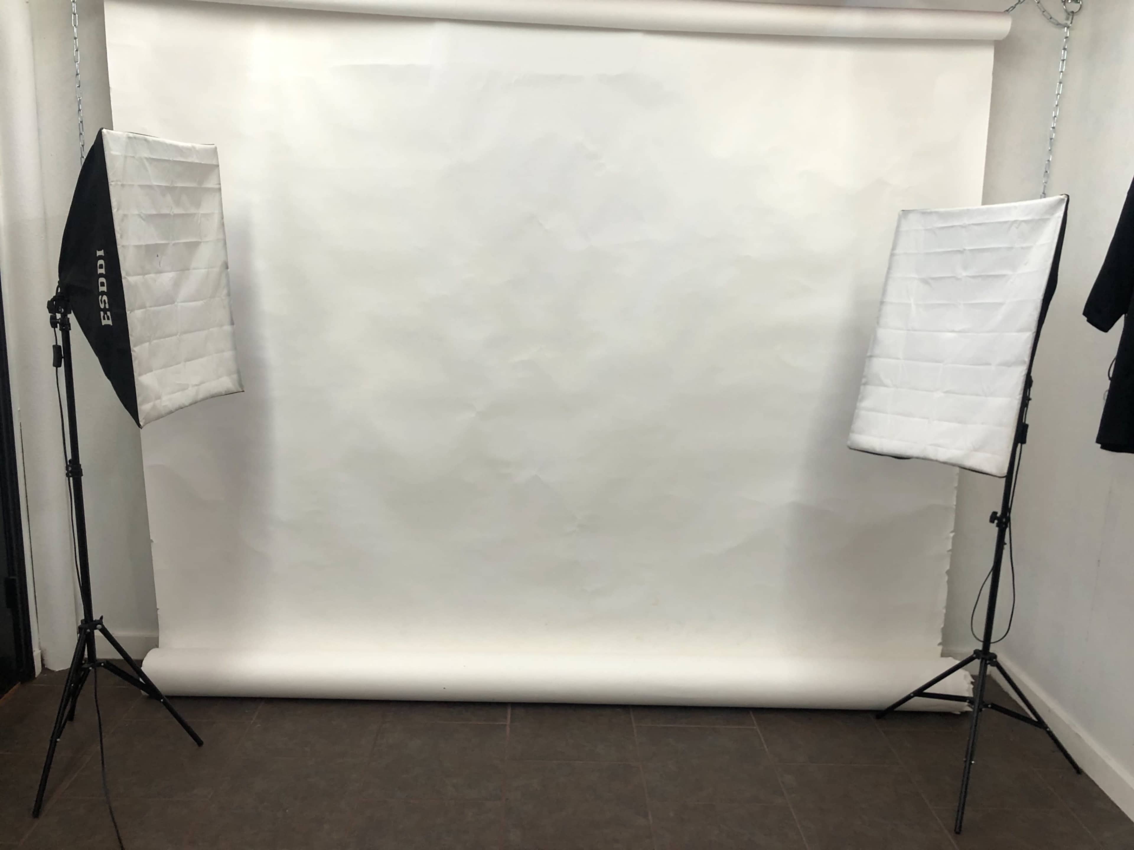 The image shows a photography studio setup with two softbox lights positioned on either side of a plain white backdrop.