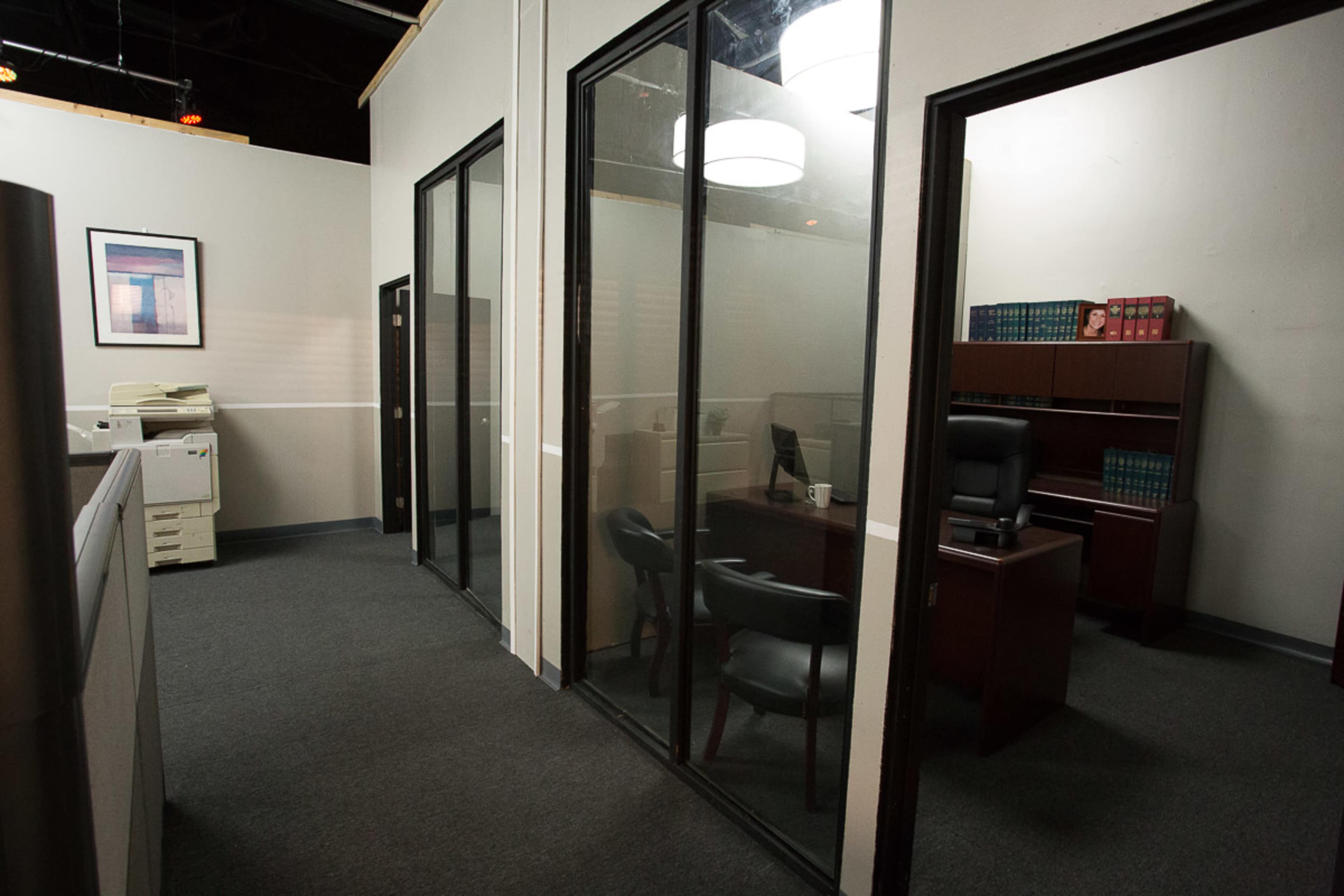 A modern office space with glass-walled meeting rooms and a desk set up in one of the enclosed areas.