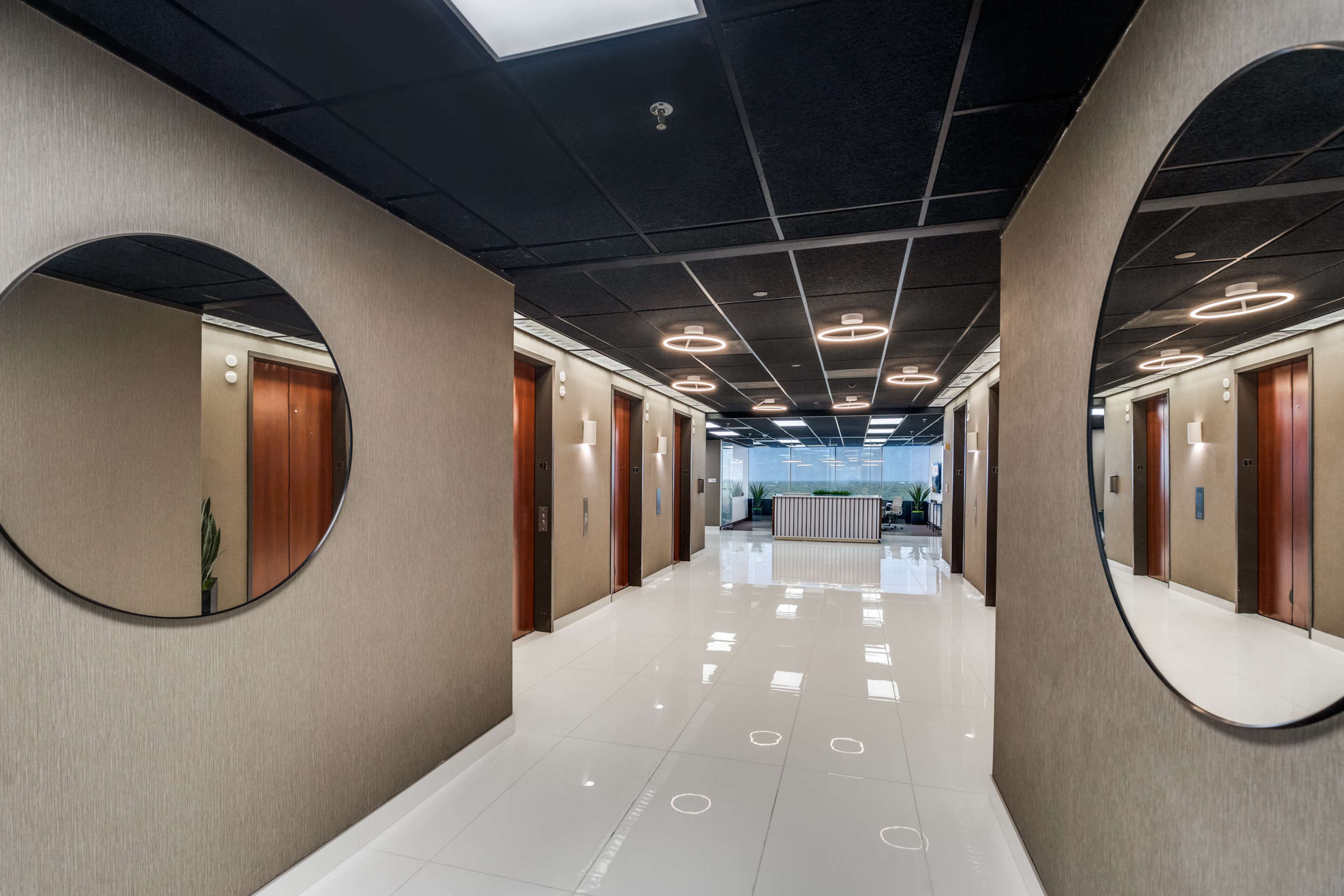A modern hallway features circular mirrors mounted on the walls, leading to a reception area at the far end.