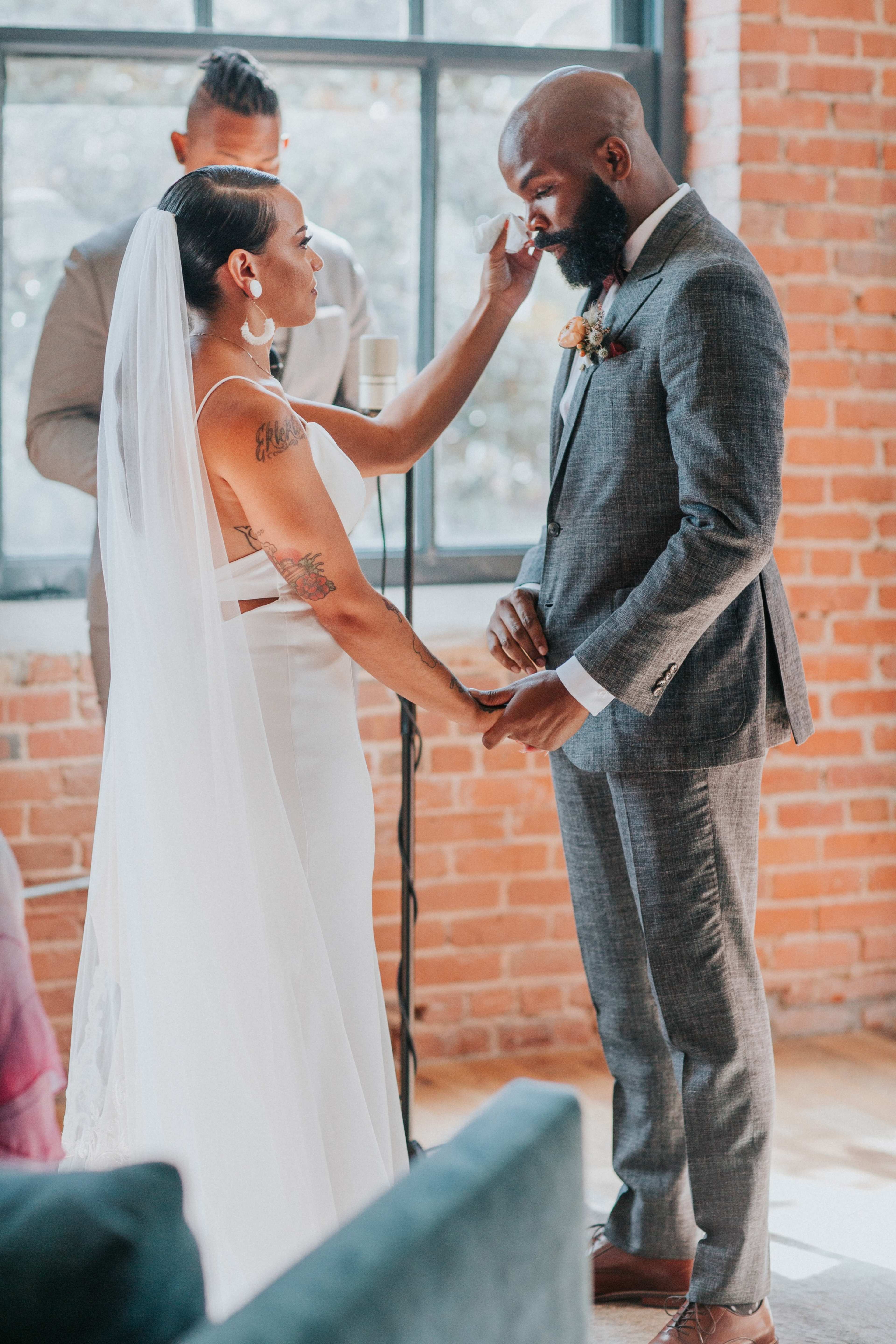 A couple exchanges vows during their wedding ceremony in a brick-walled venue.