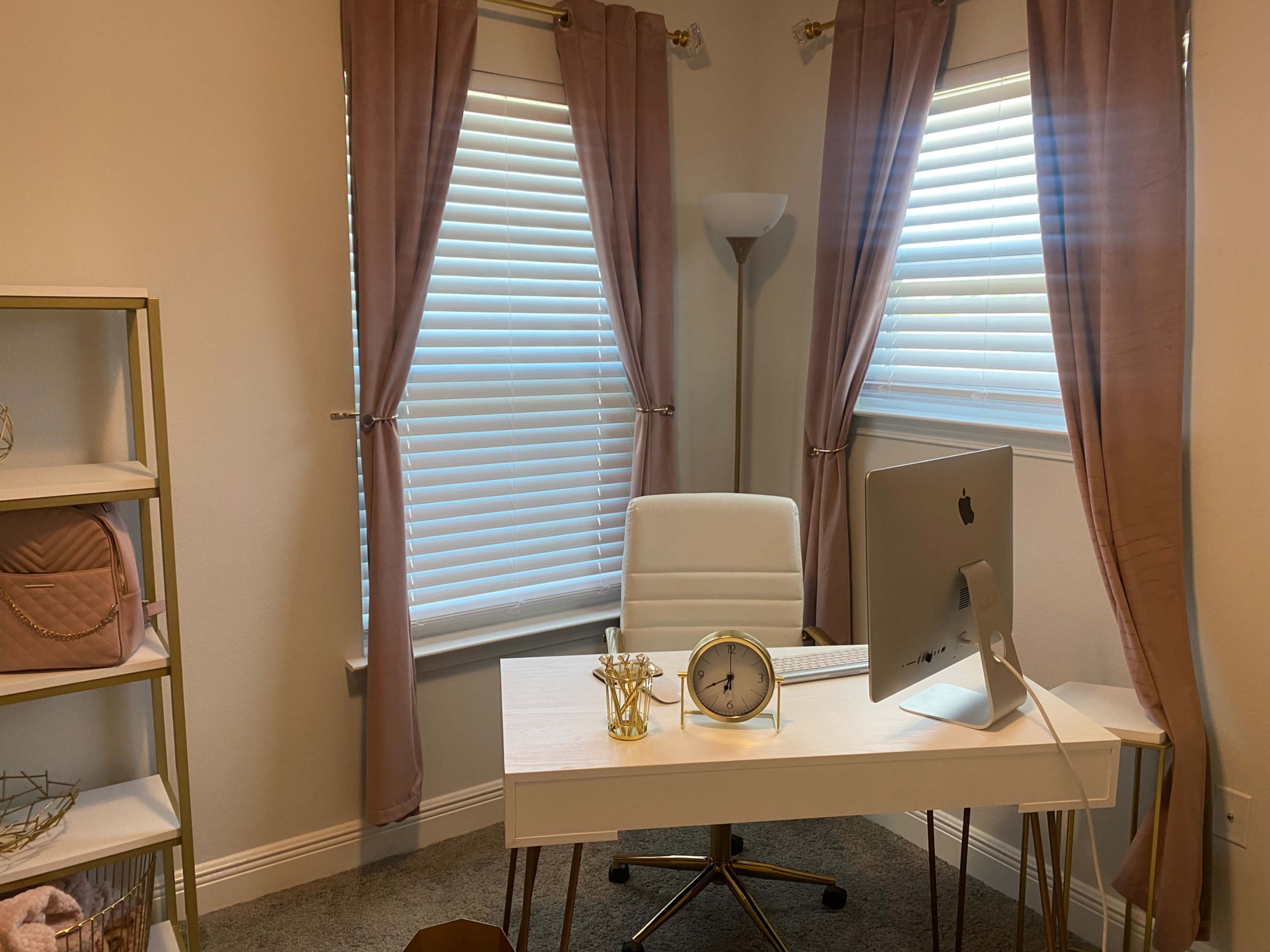 A well-organized home office with a white desk, a computer, and soft curtains framing two windows.