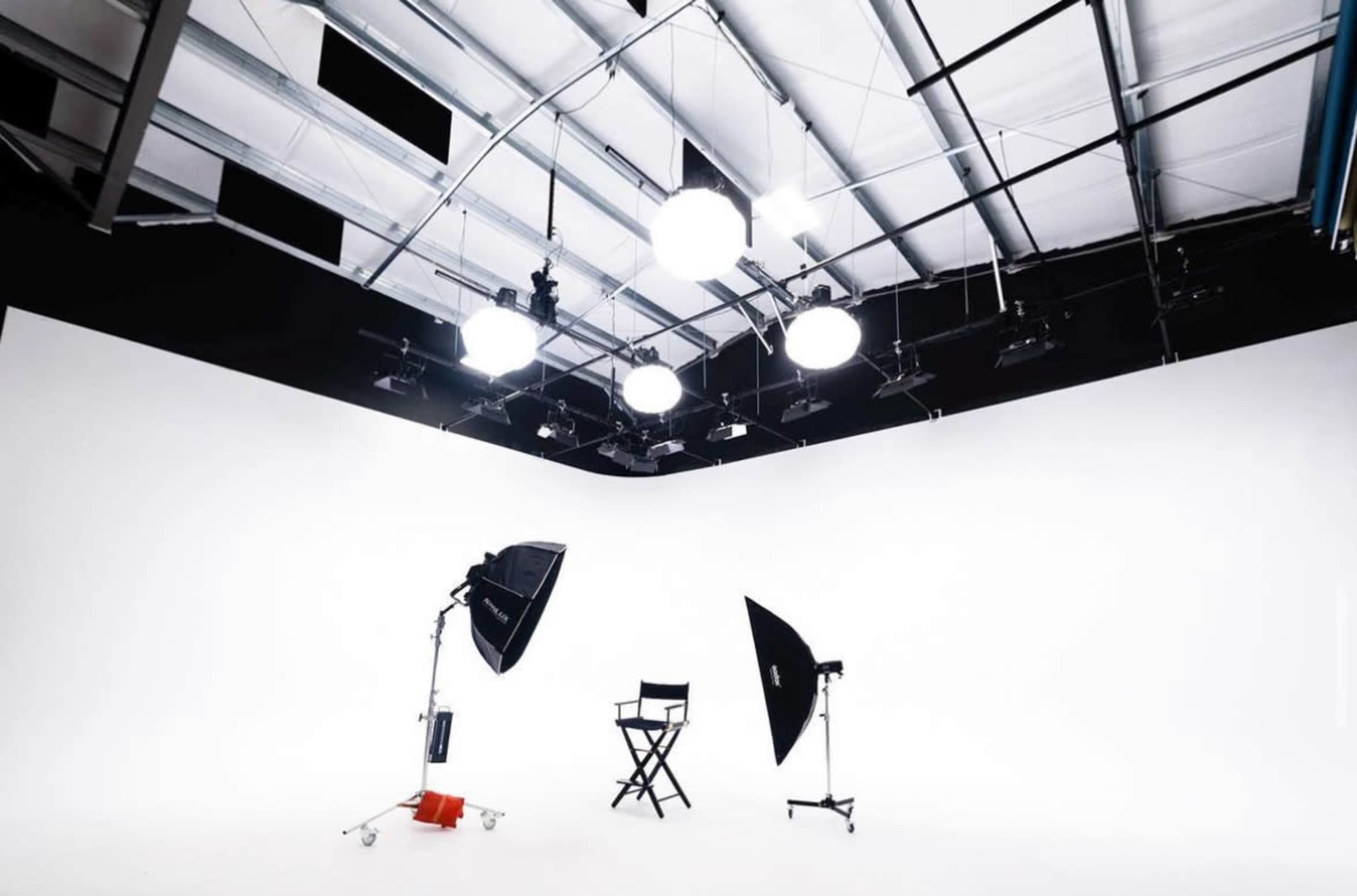 A photography studio features a white background, a director's chair, and multiple lighting equipment arranged around the space.