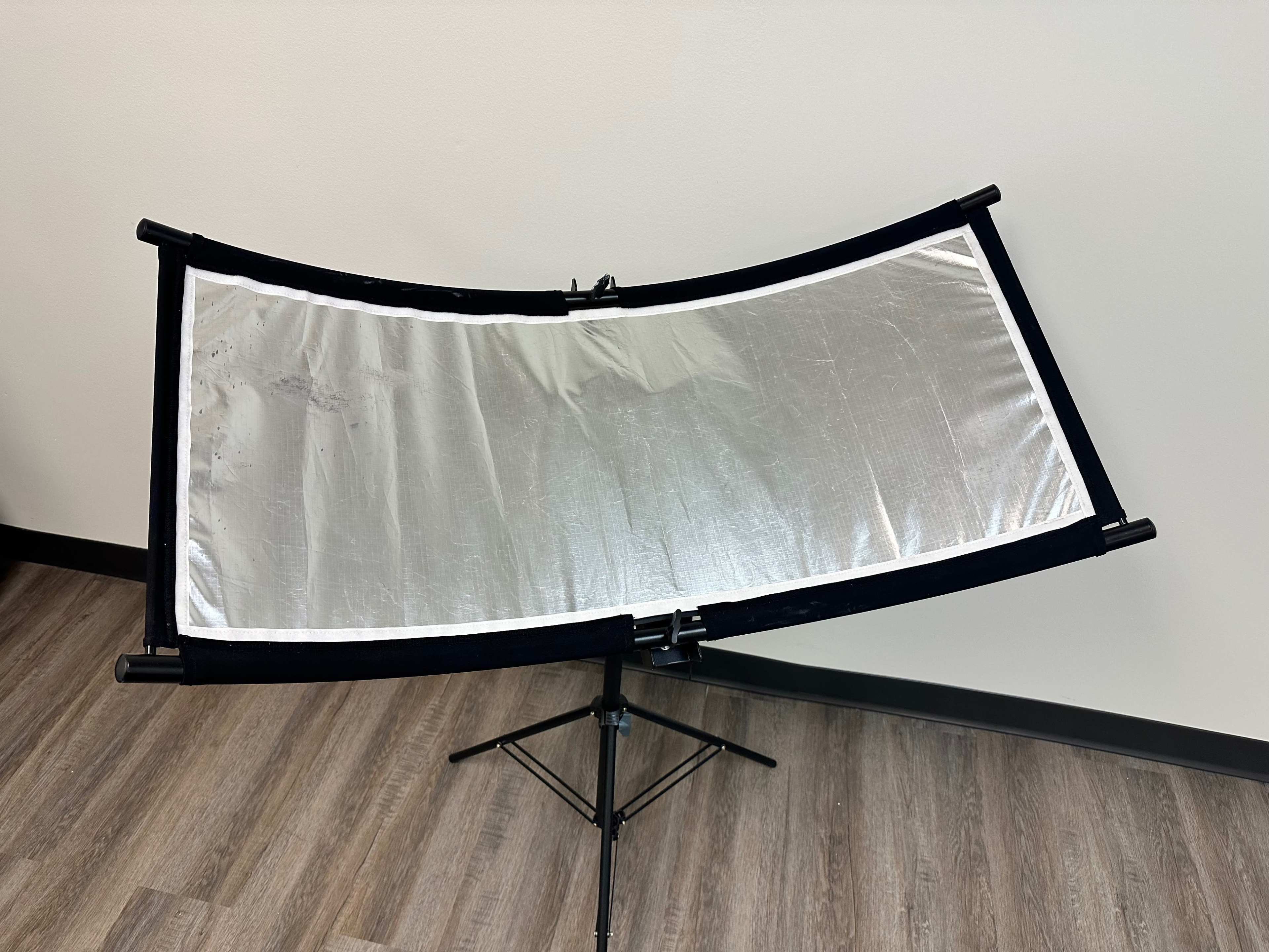 A reflective lighting panel is mounted on a tripod in a room with a wood floor.