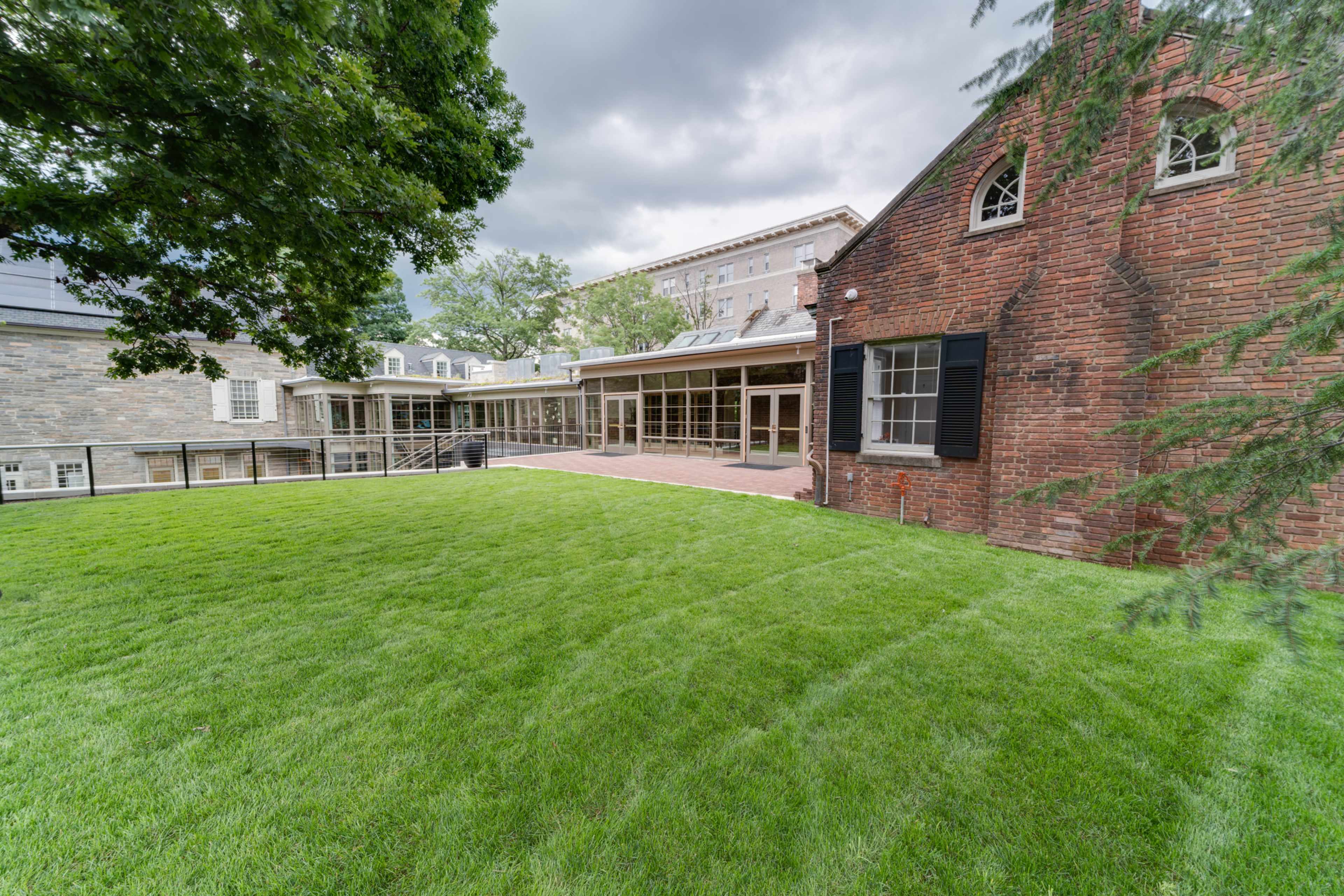 A grassy lawn surrounded by brick and stone buildings under a cloudy sky.