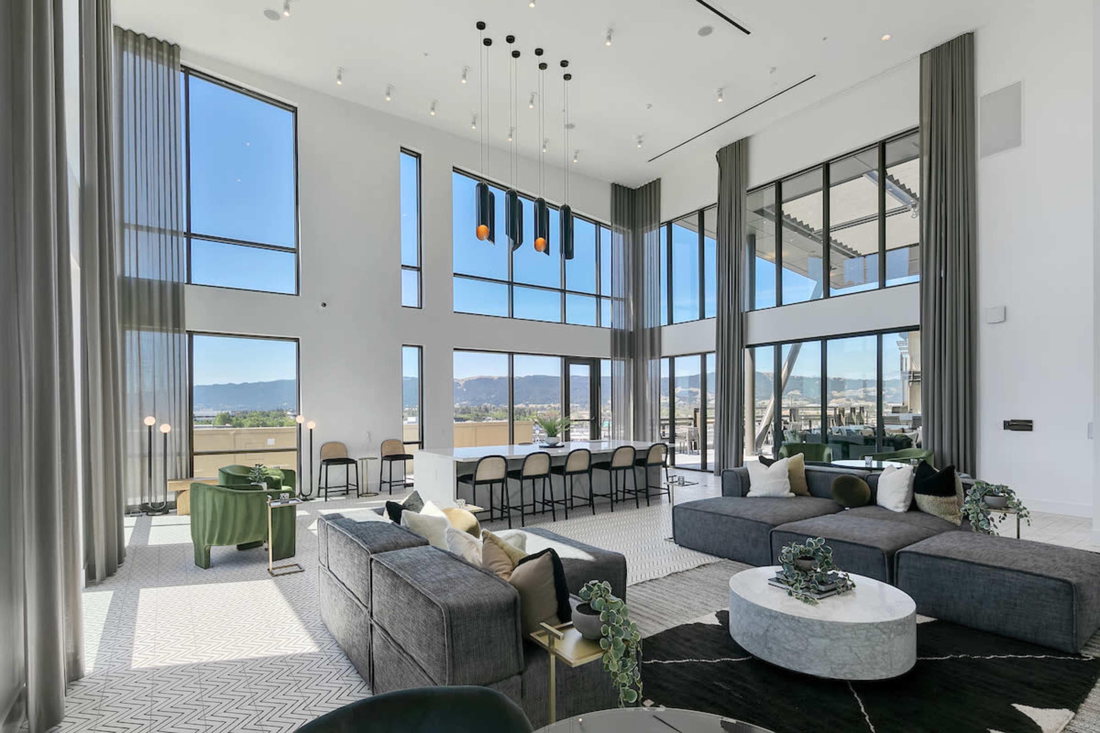 A spacious living area with large windows overlooking a view and modern furnishings, including a circular coffee table and two dark sofas.