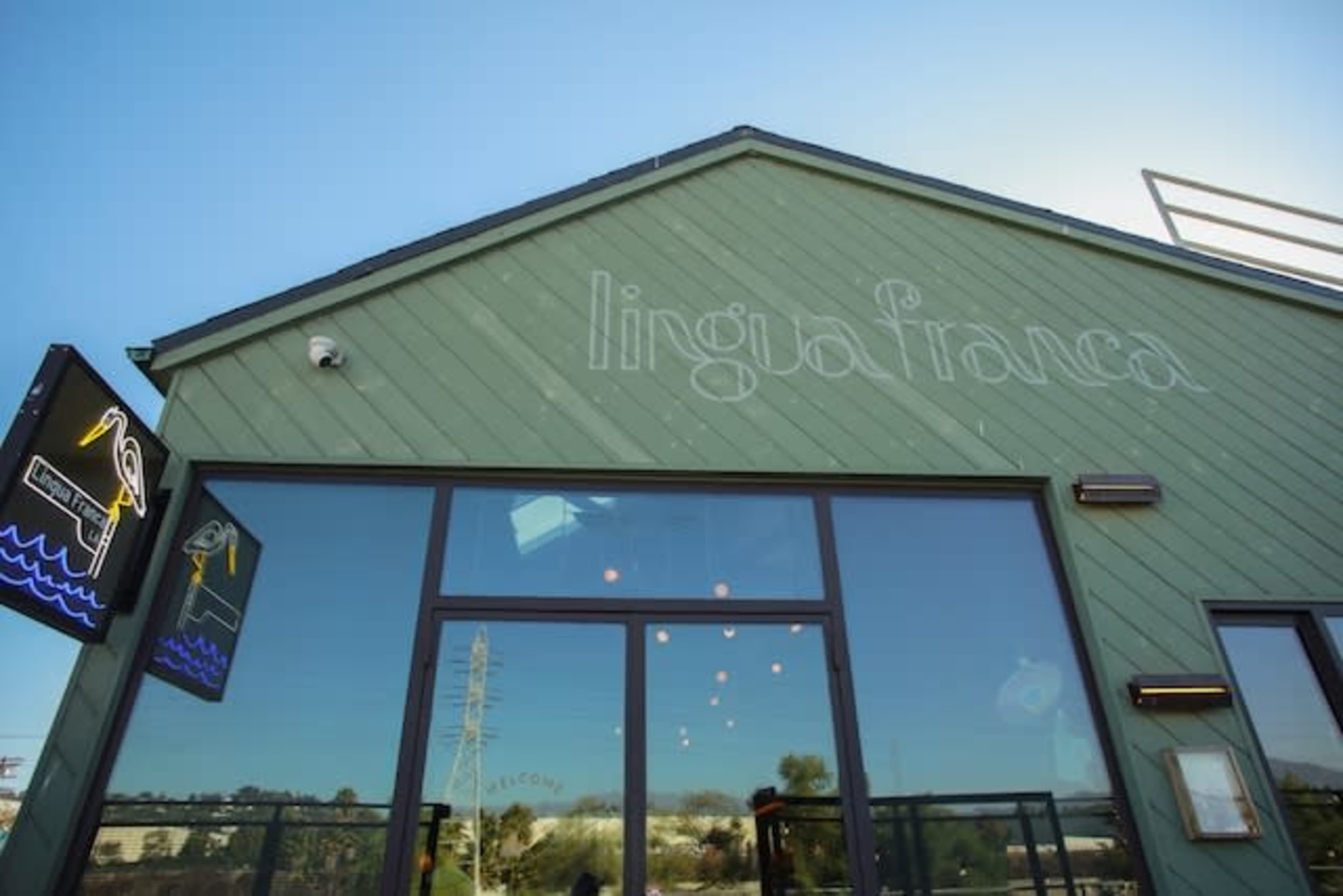 The image shows the exterior of a green building with the name "lingua franca" etched on the wall and large glass windows.