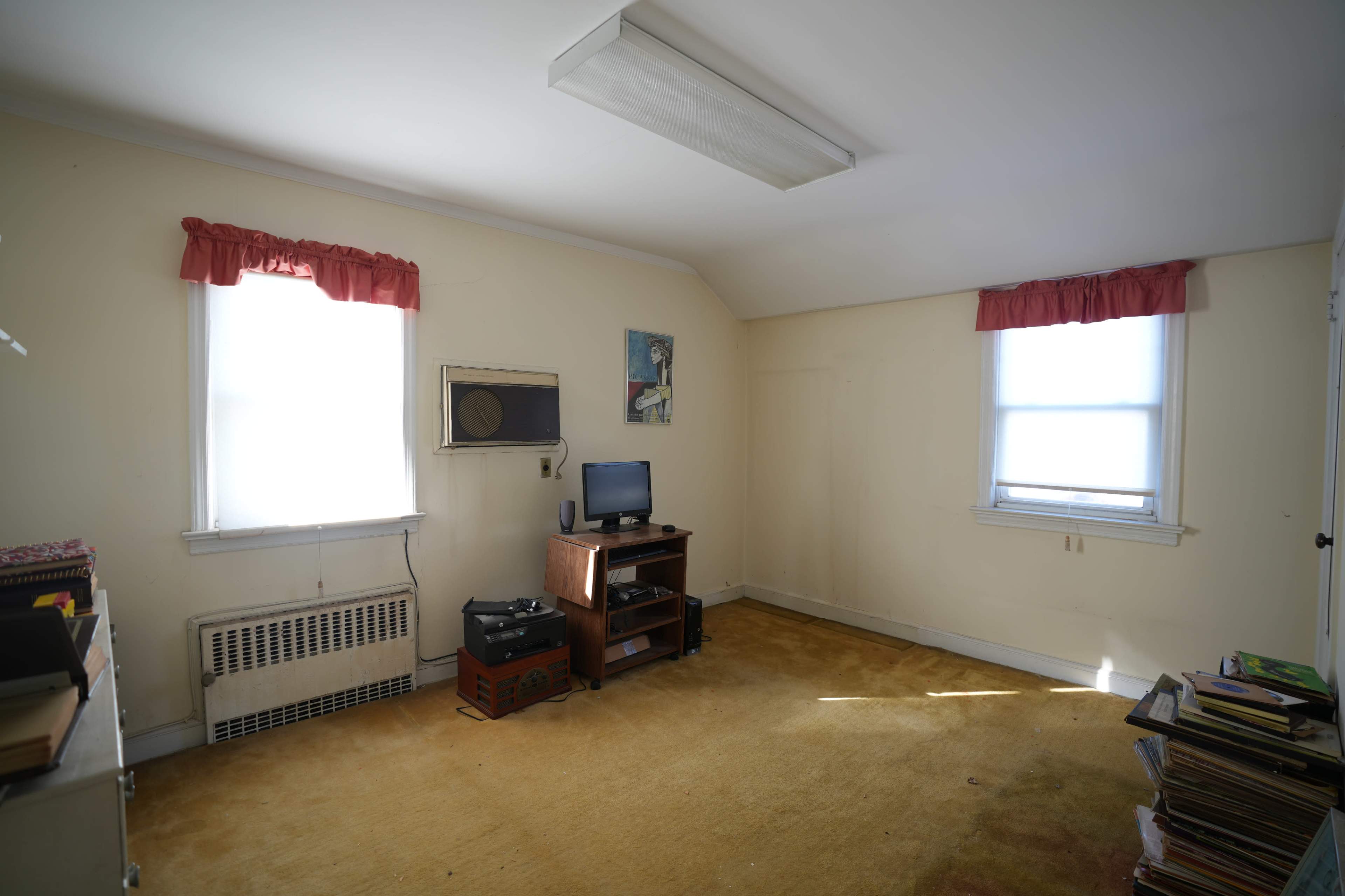 The room features two windows, a television on a wooden stand, and various books and magazines on the floor.