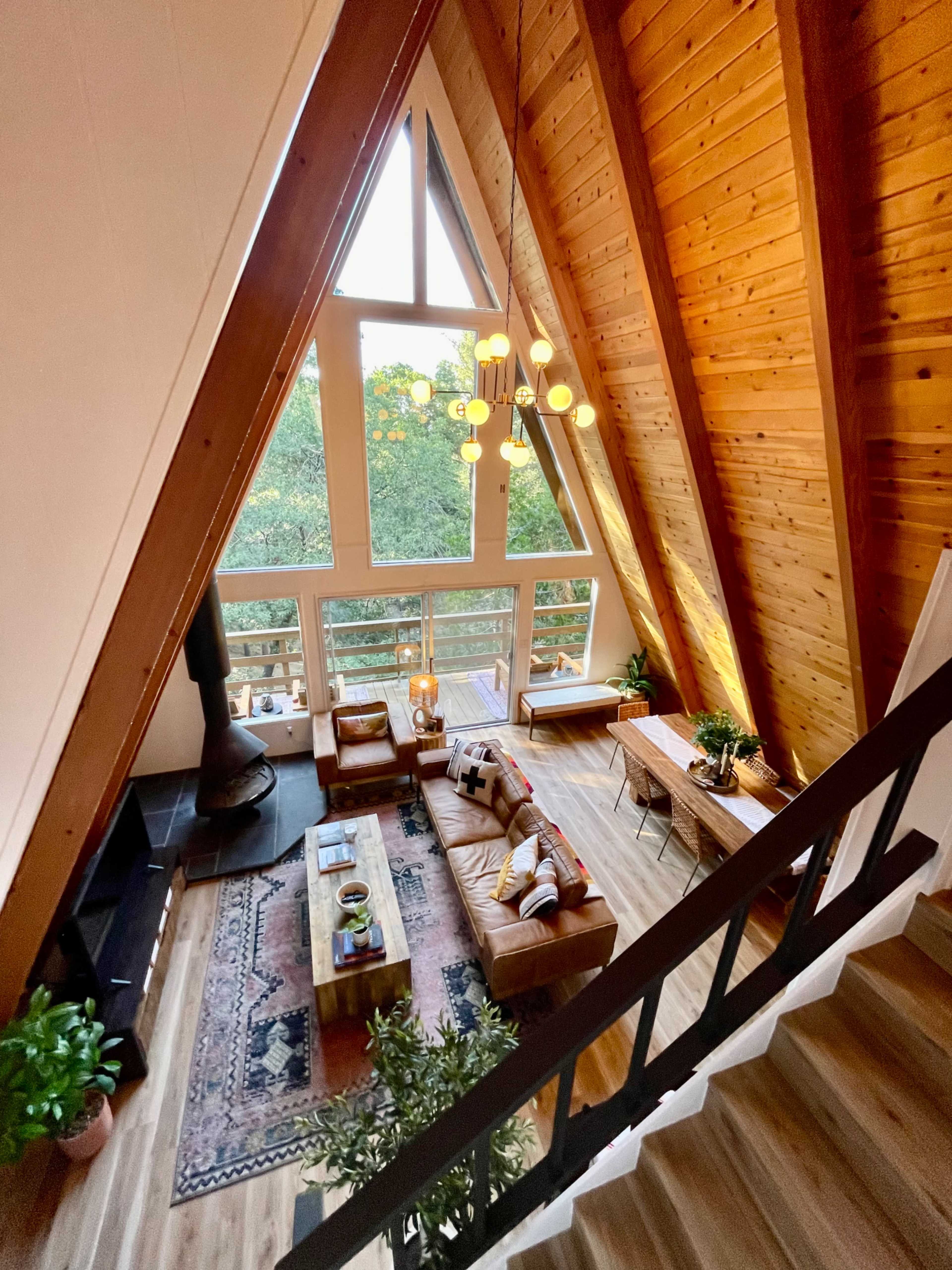 A cozy A-frame living room with wooden walls, large windows, and a comfortable seating area centered around a coffee table.