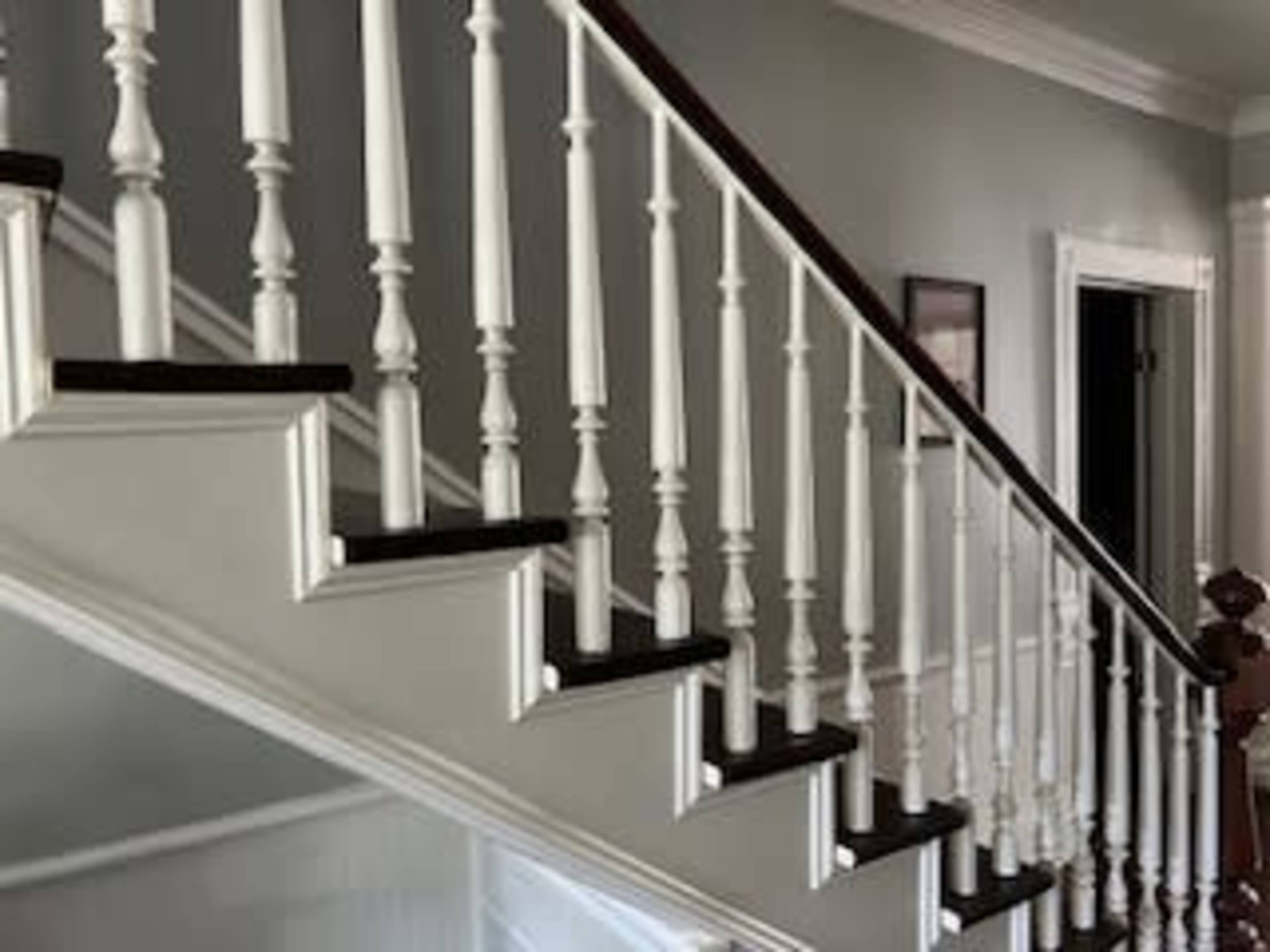 The image shows a staircase with white balusters and dark wooden treads, leading to an upper level in a well-lit hallway.