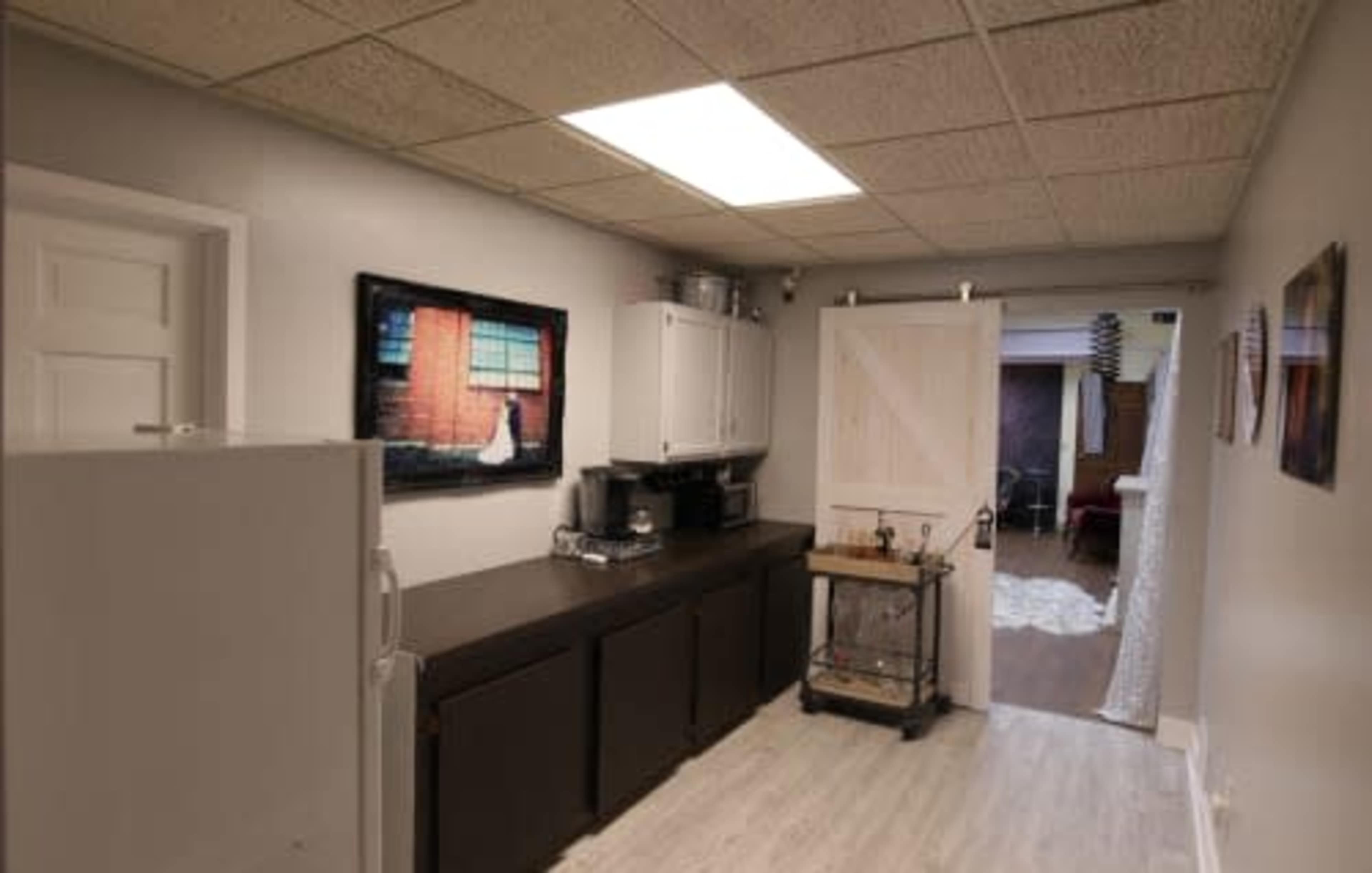A kitchen with a refrigerator, a long black countertop, a white cabinet, and a door leading to another room.