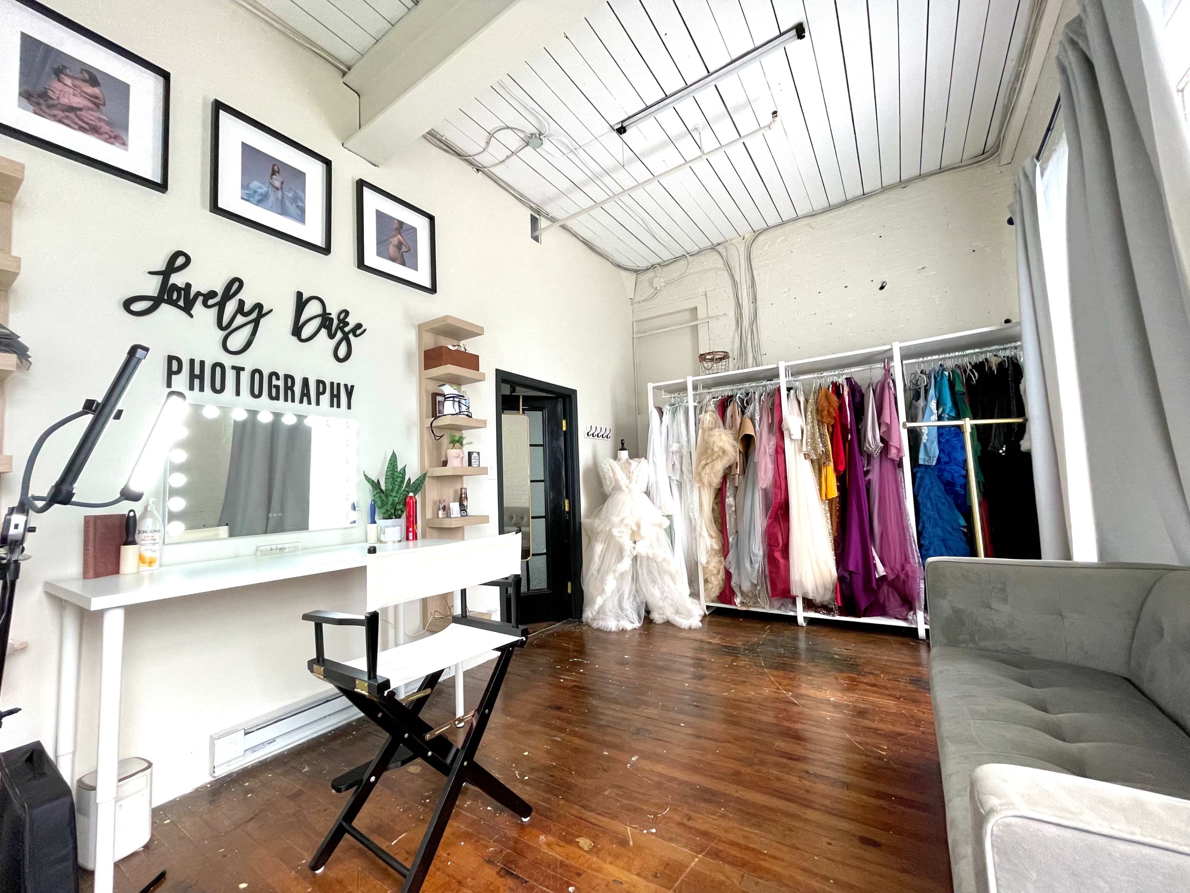 A photography studio with a makeup station, a couch, and a rack displaying various colorful dresses.