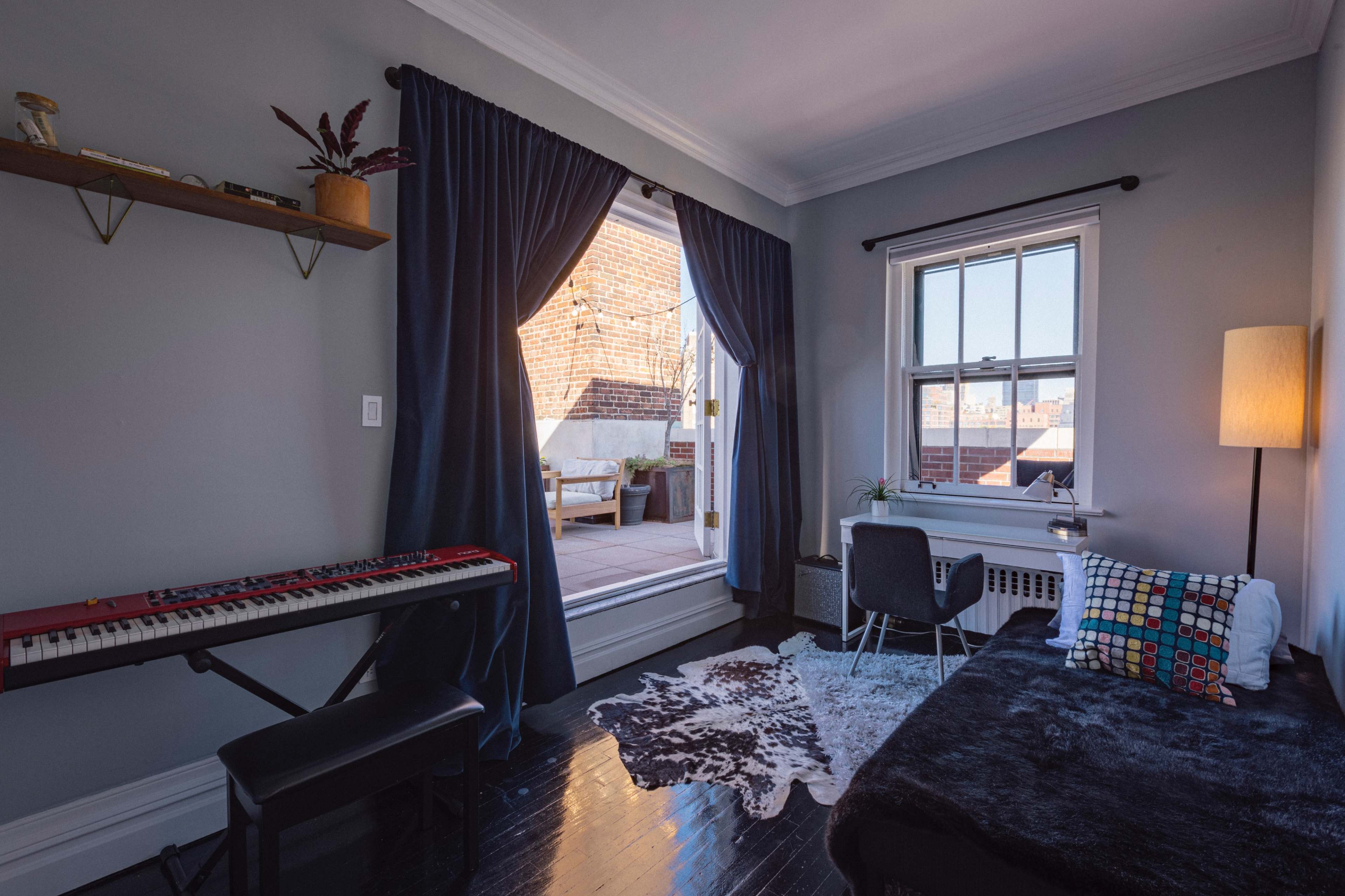 A small room features a keyboard, a chair, and a doorway leading to a sunny outdoor terrace.