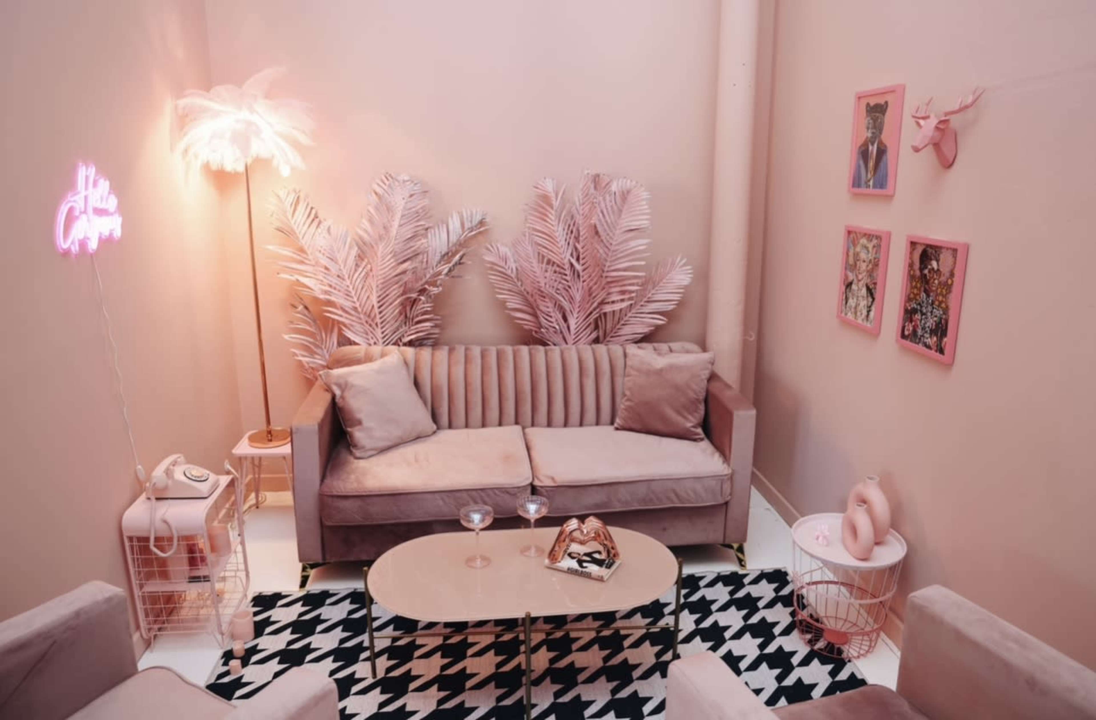 The scene features a cozy pink-themed lounge area with a sofa, patterned rug, and decorative plants.