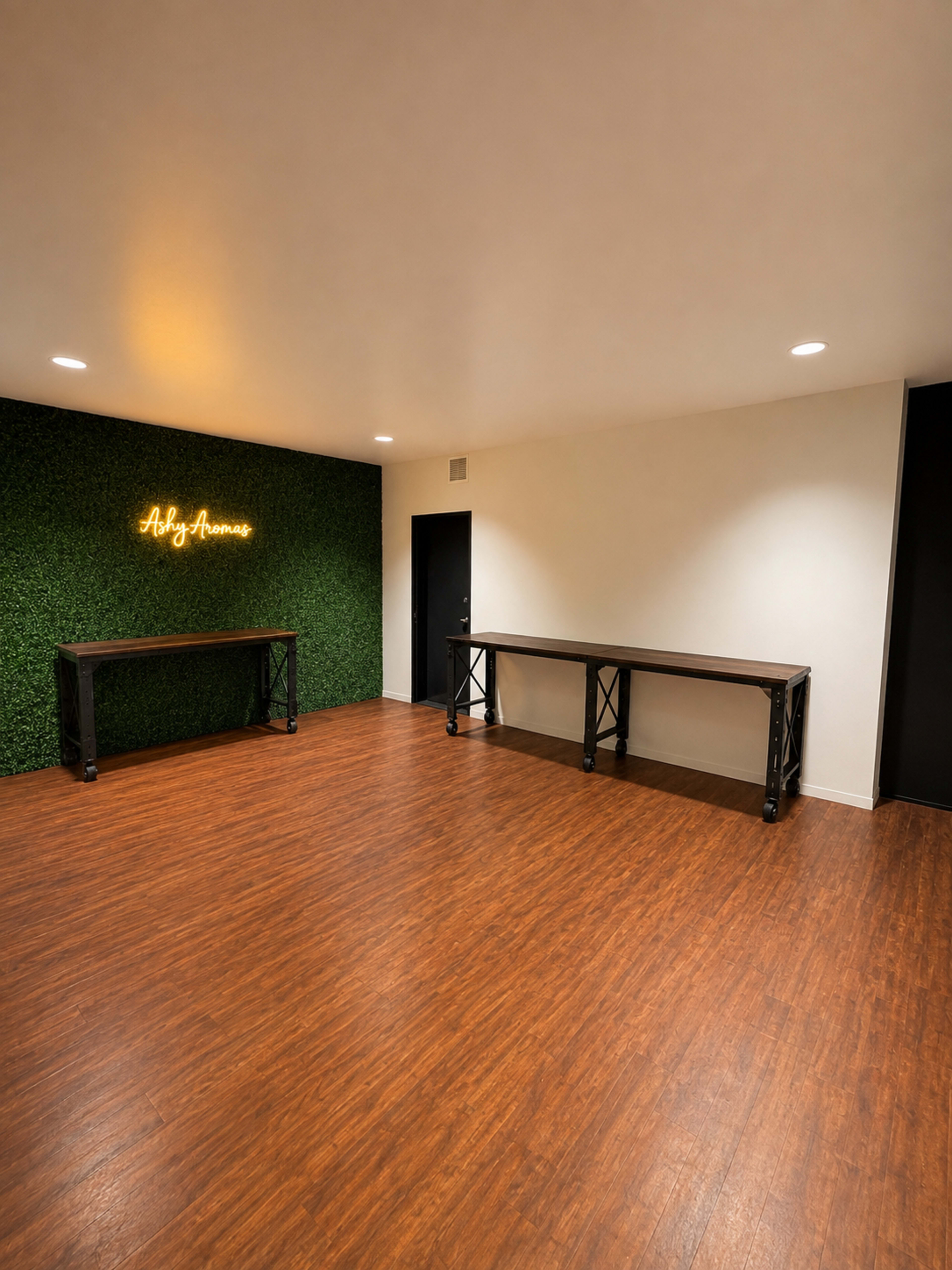 The image shows a spacious interior room with wooden flooring, two black tables against the wall, and a green wall with a neon sign reading "Asty Avenue."