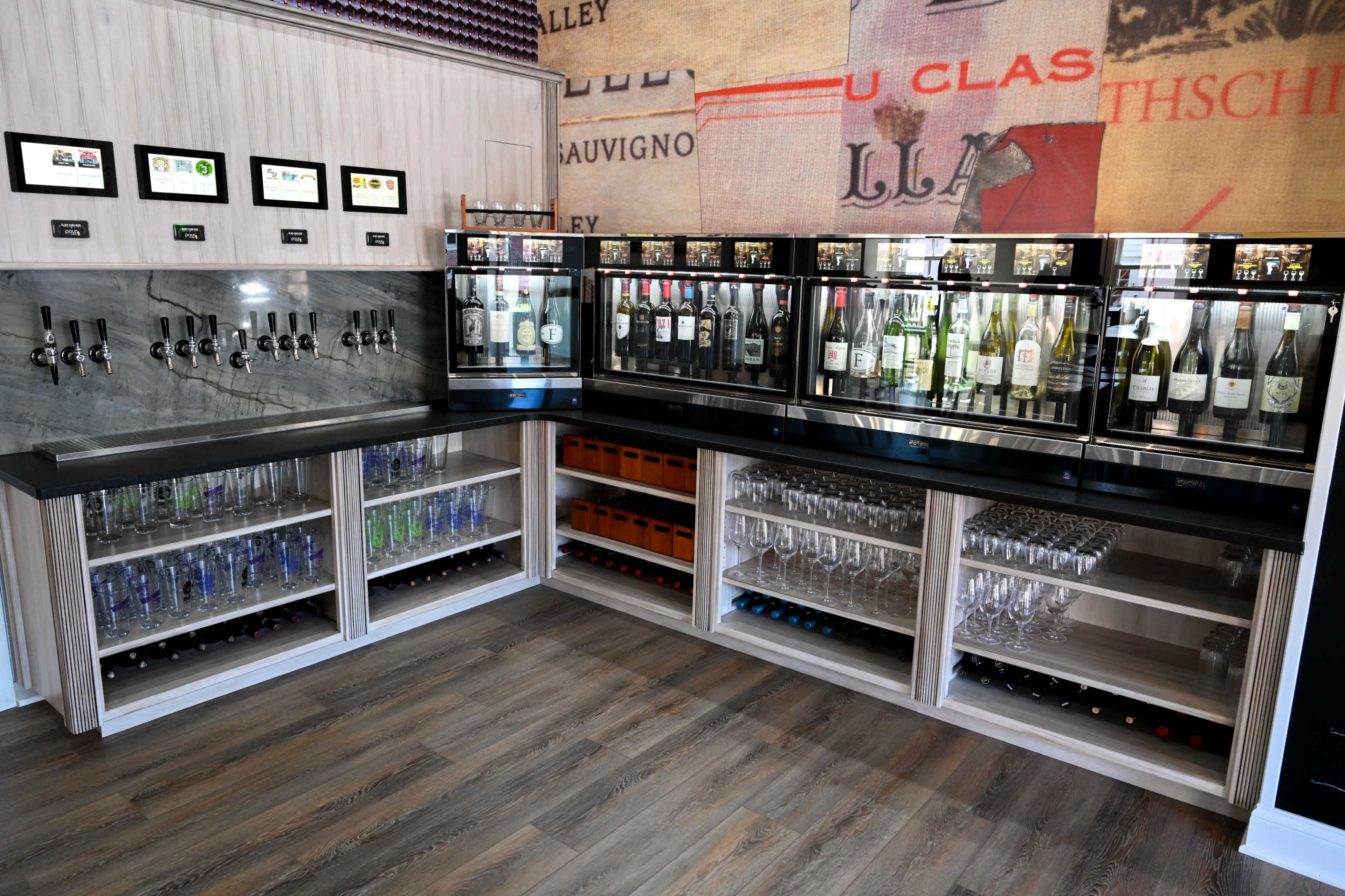A modern bar area featuring multiple beverage taps, glass storage, and an array of wine bottles displayed in glass cabinets.