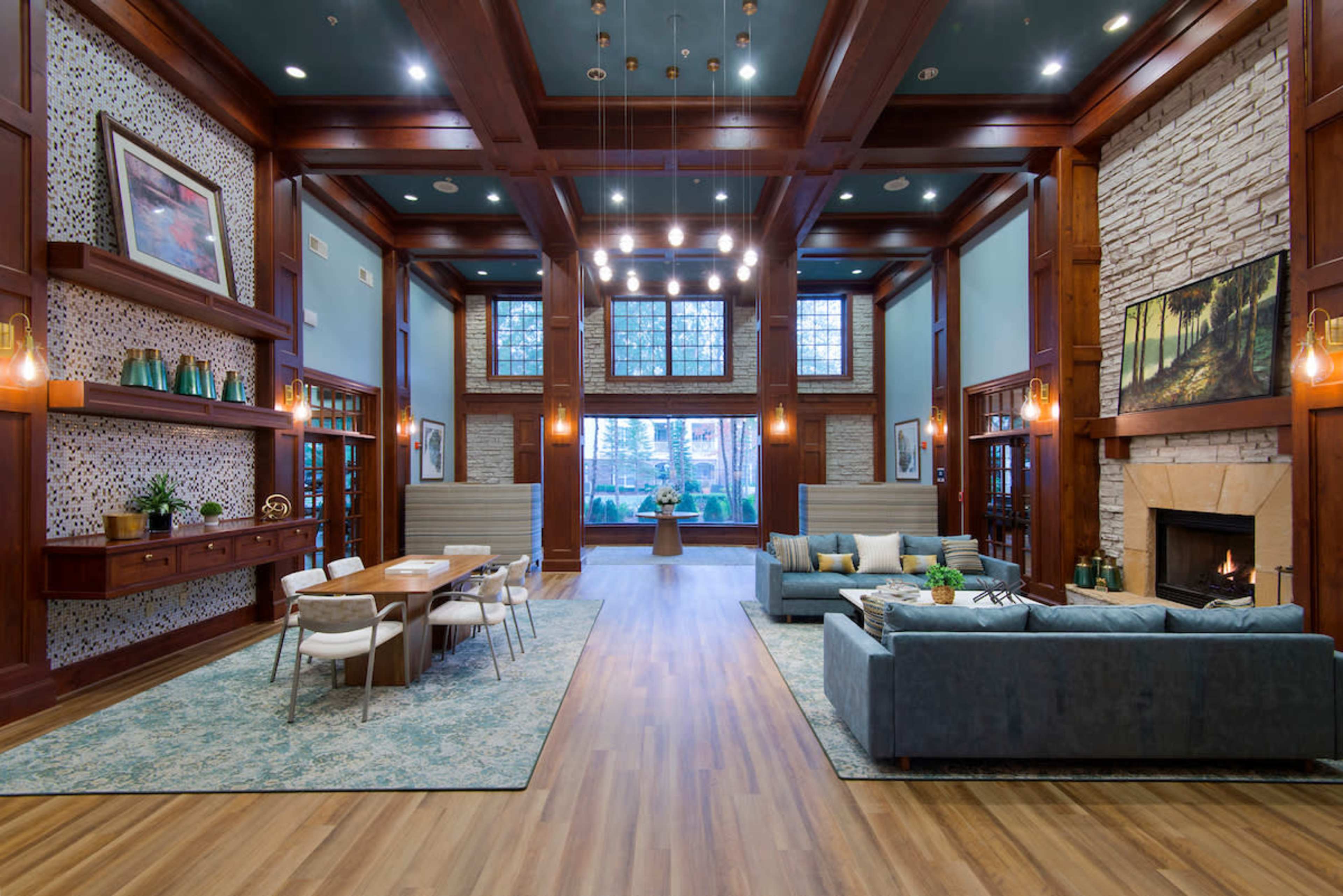 The image shows a spacious living room with wooden beams, a stone fireplace, and a dining area featuring a large table and modern furniture.