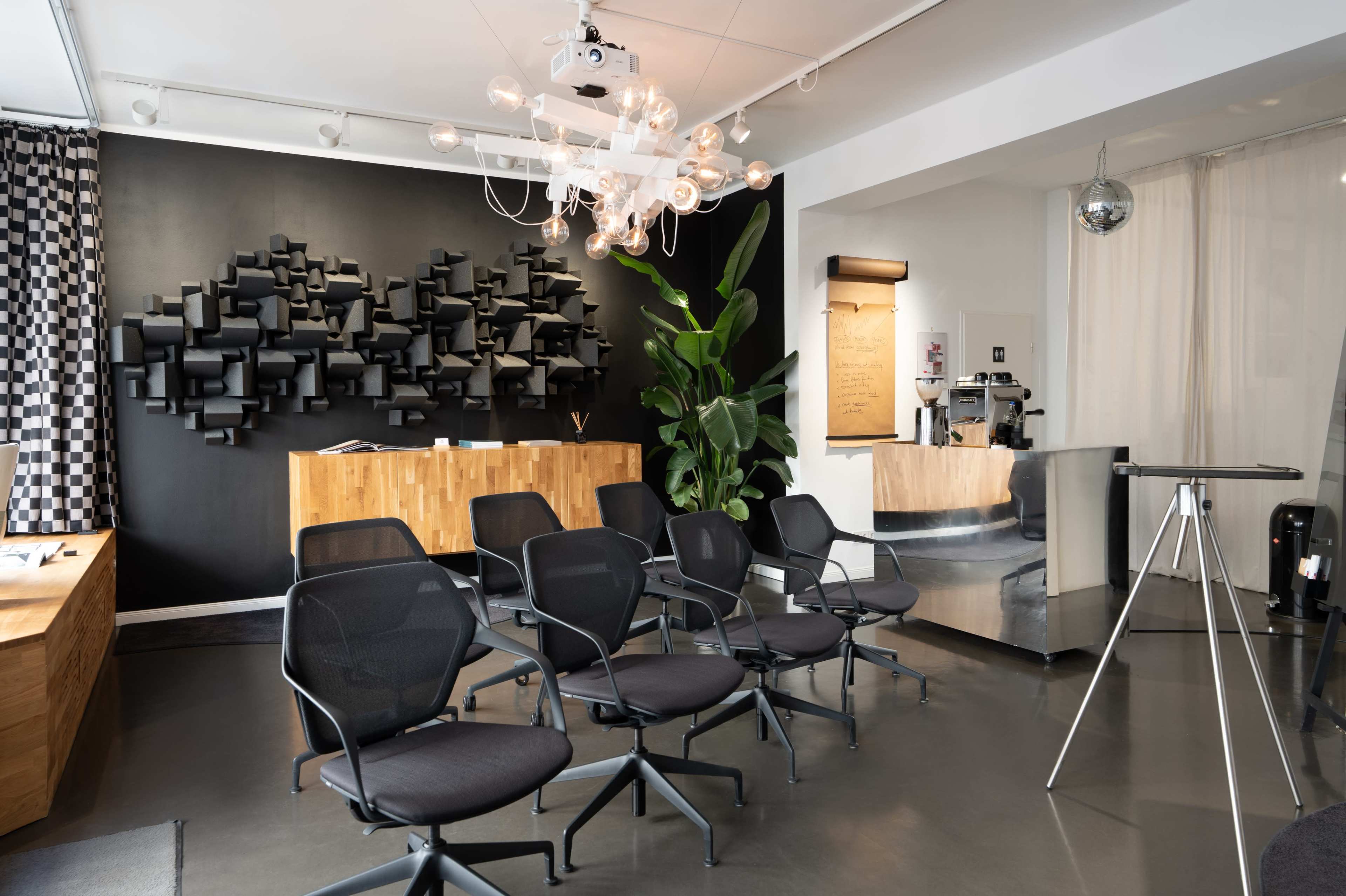 The image shows a modern reception area with dark walls, stylish seating, and a large artistic installation made of black panels.