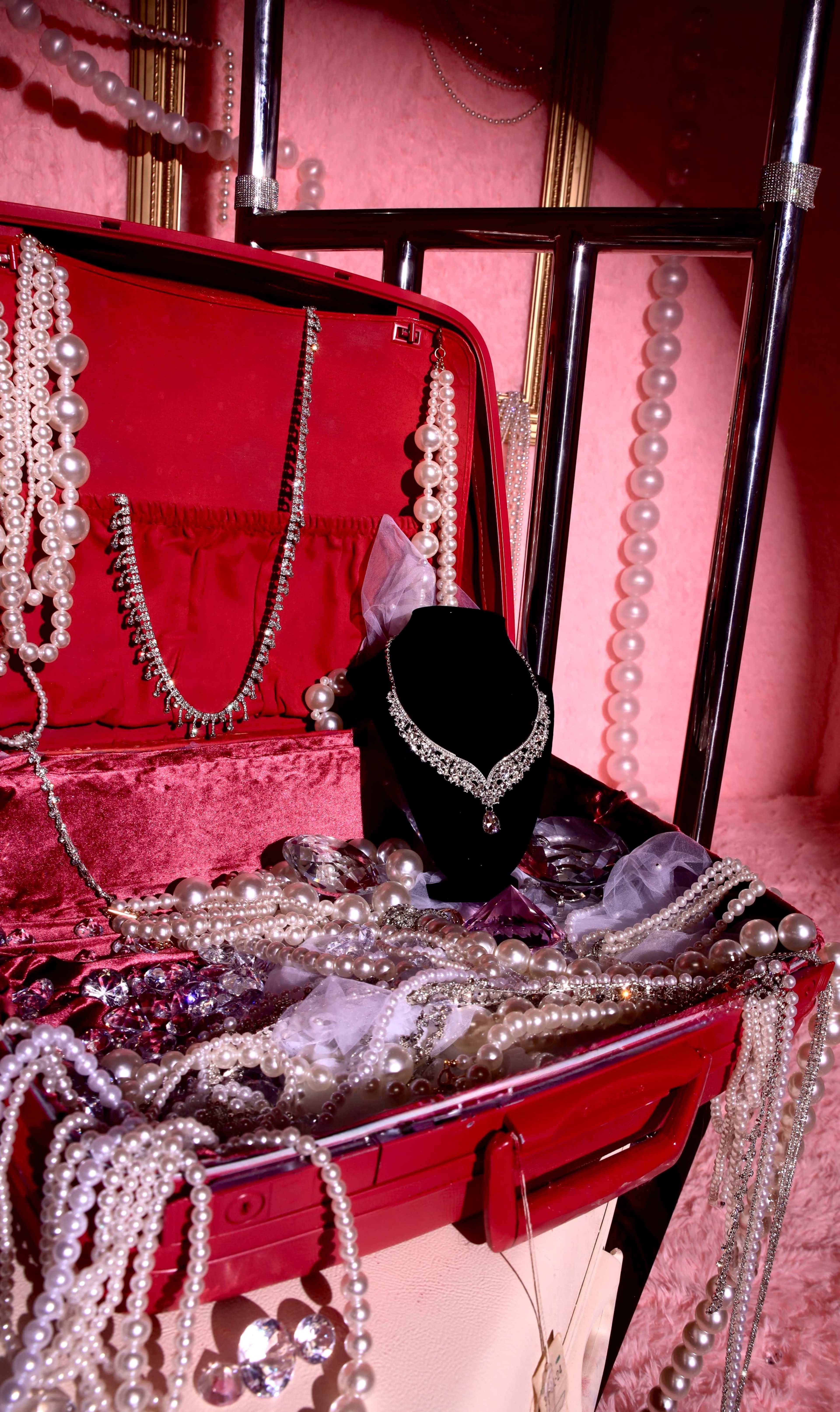 A red suitcase is filled with various strands of pearls and a necklace displayed on a black velvet stand.