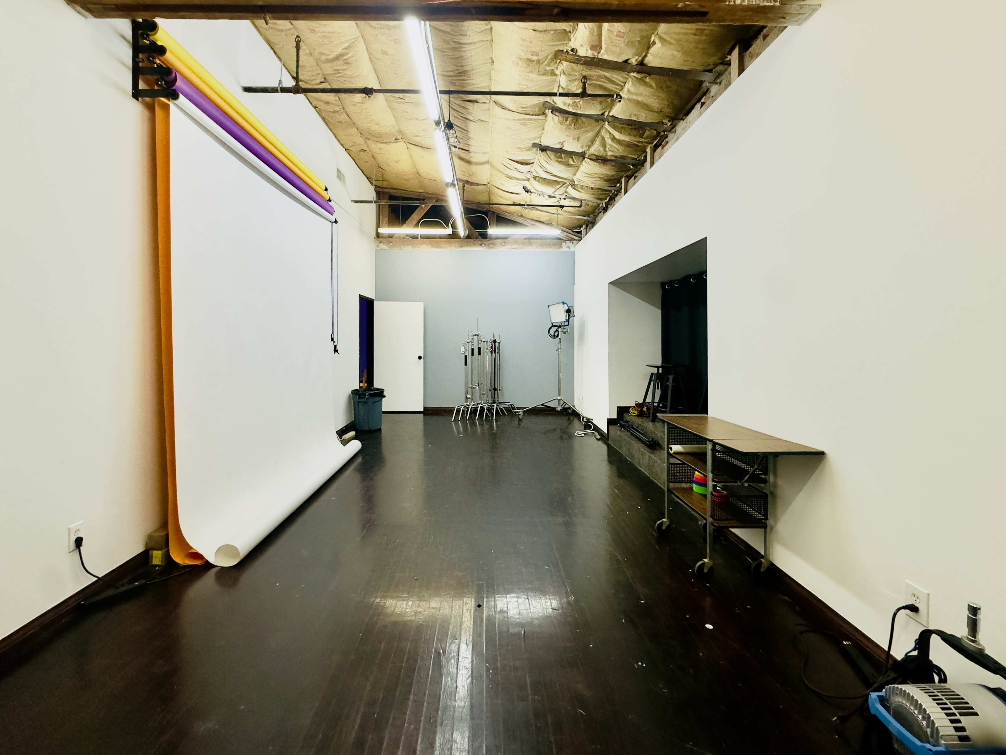 The image shows a spacious studio with a large seamless backdrop, a mirrorless wall, and various photography equipment set up along one side.