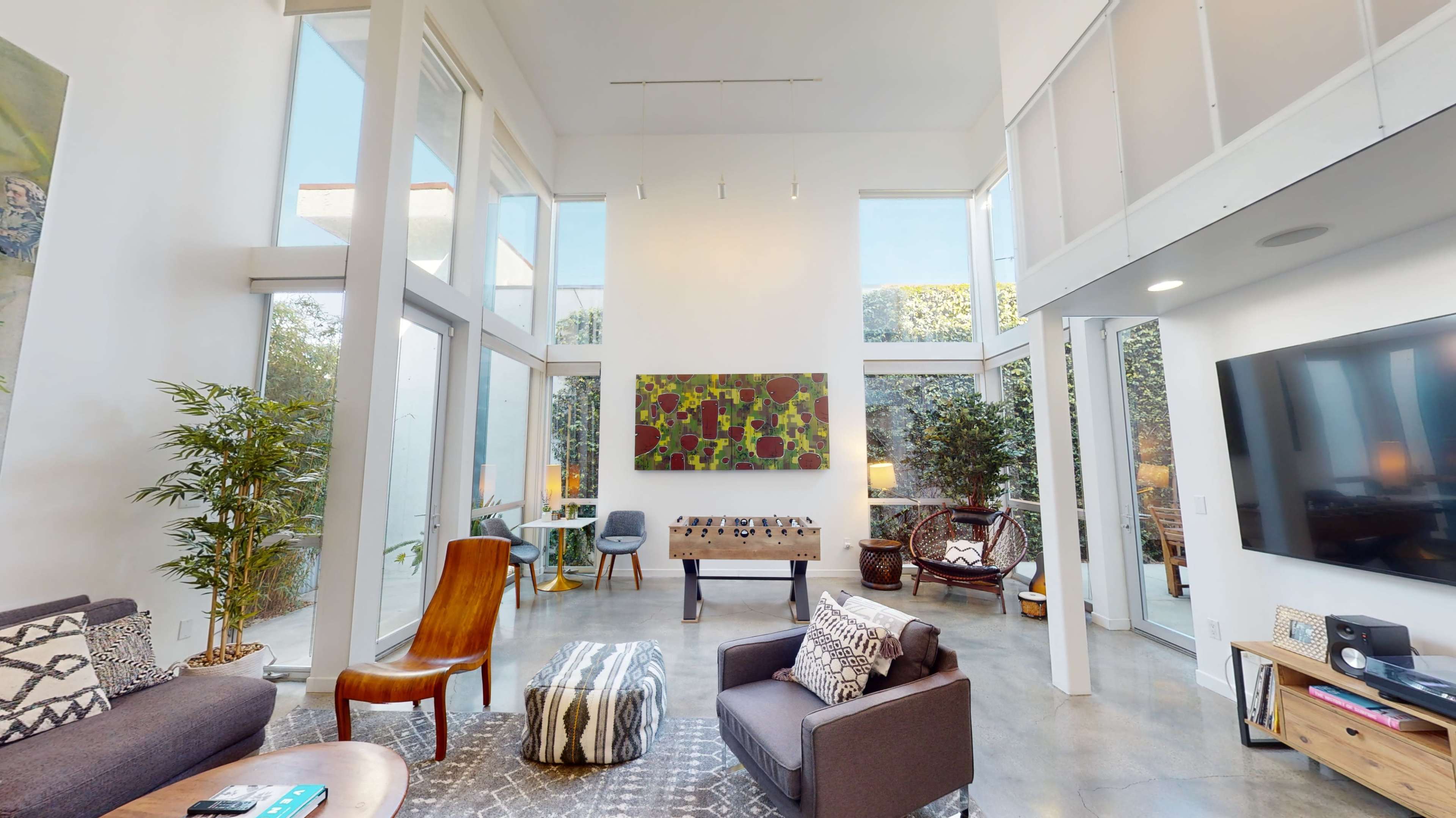 A modern living room with tall windows, a large artwork on the wall, and various seating options arranged around a coffee table.