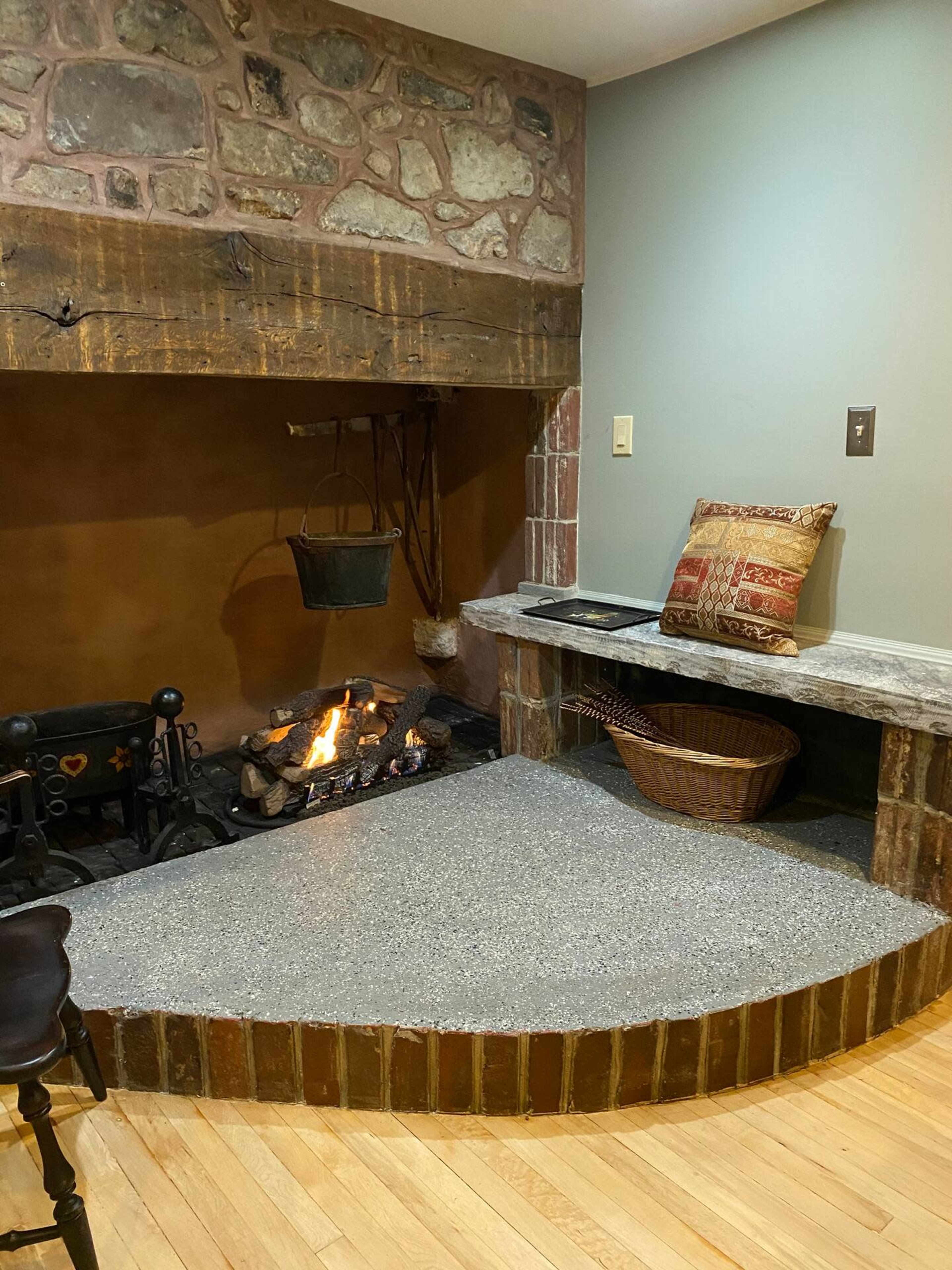A corner fireplace with a stone wall, a metal bucket hanging, and a granite countertop beside a woven basket.