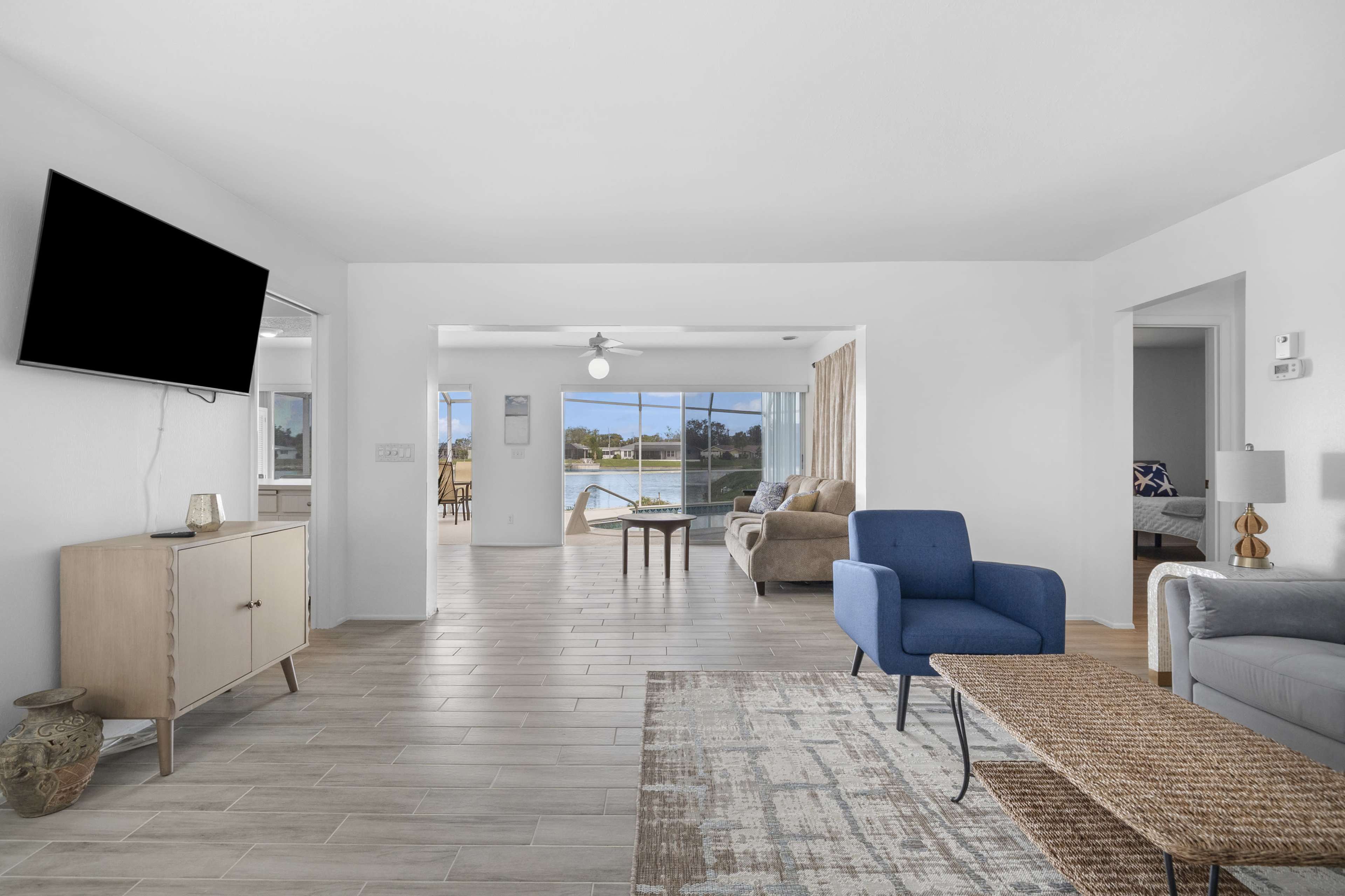 A modern living room with a blue armchair, a coffee table, and a TV mounted on the wall, leading to a view of a large window with natural light.