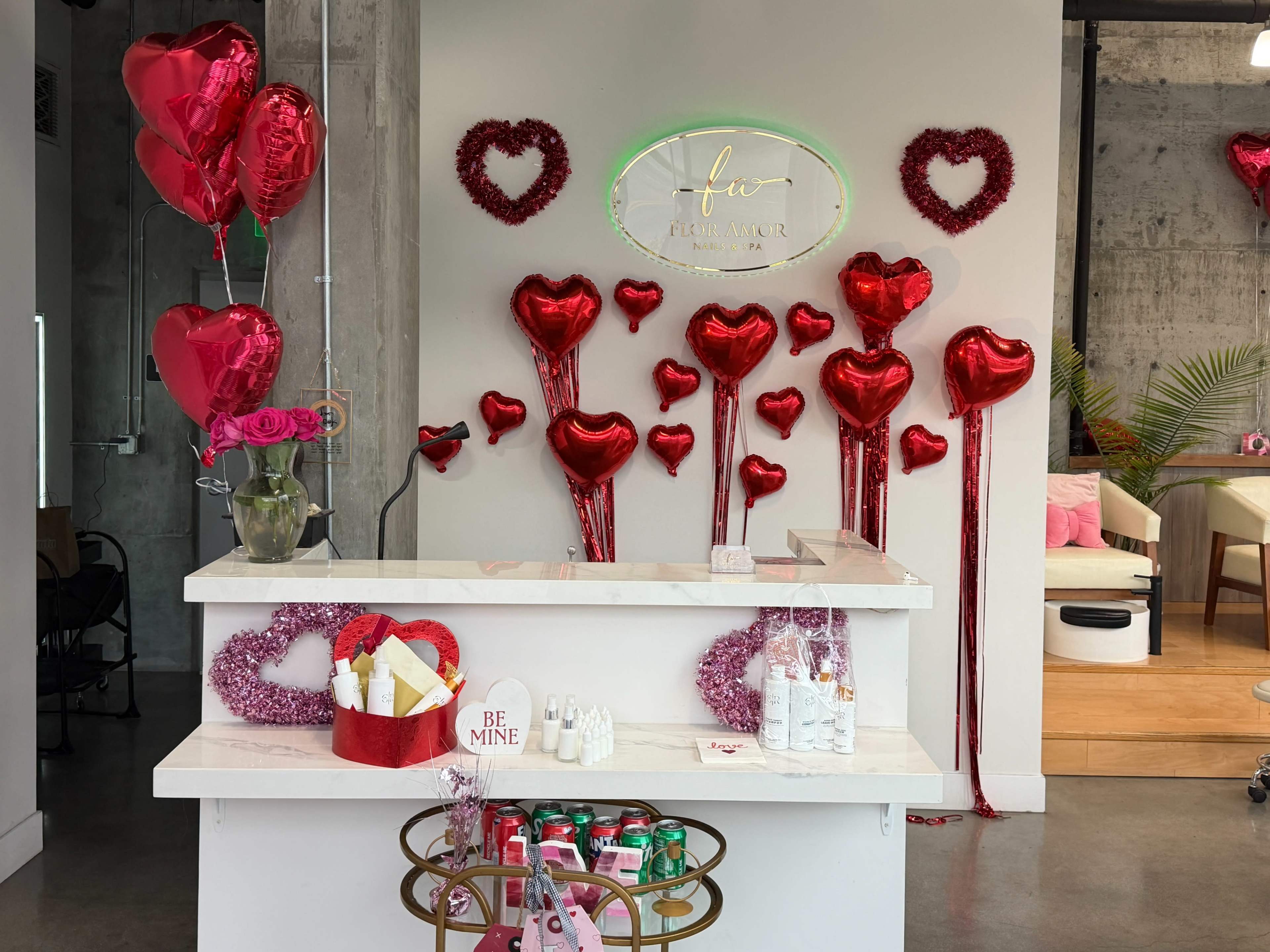 A reception area features a white counter adorned with Valentine's Day decorations, including red heart-shaped balloons and a "BE MINE" sign.