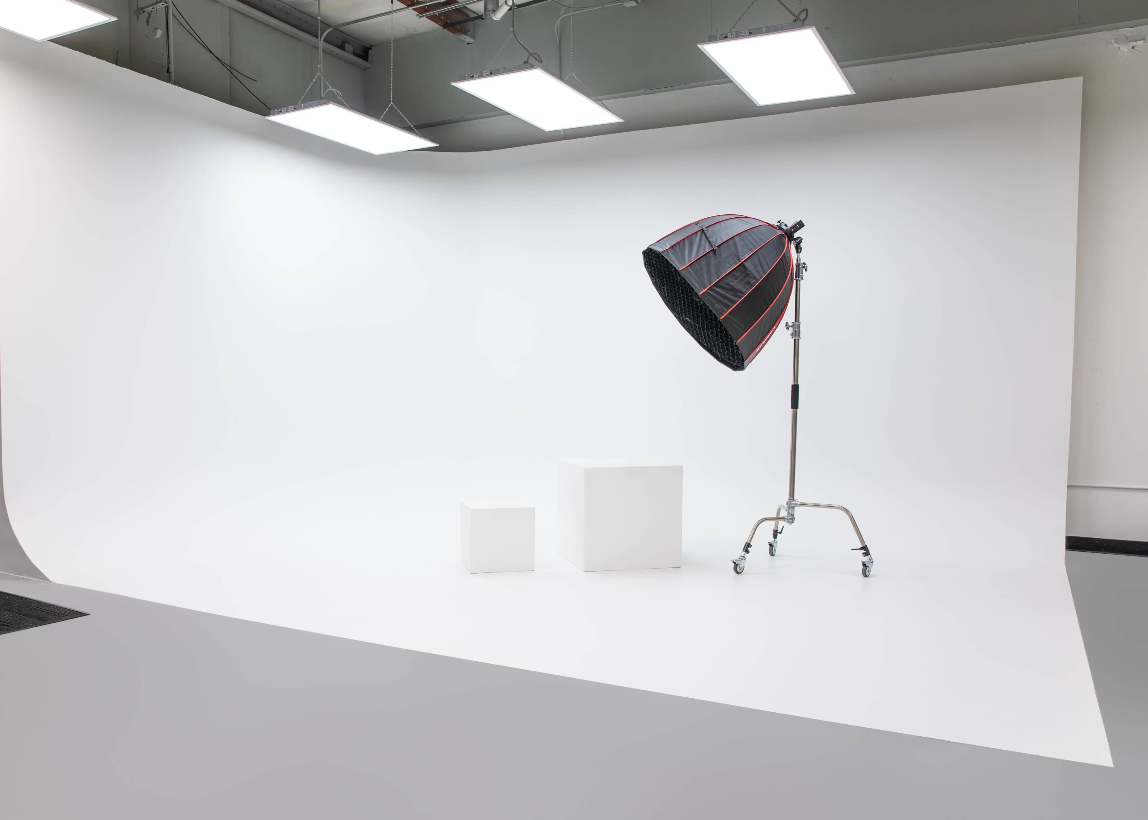 A photography studio with a white backdrop, two white blocks, and a large light fixture on a stand.